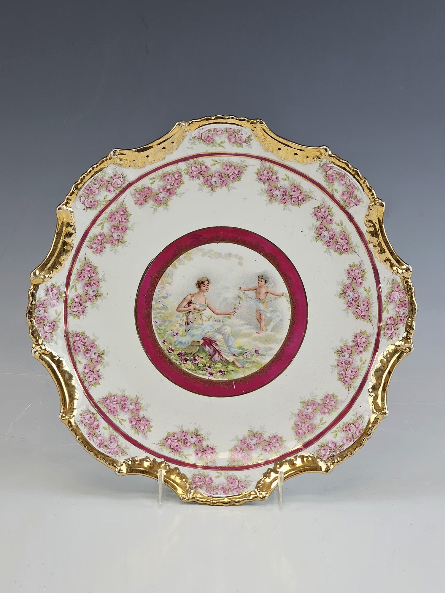 ANTIQUE AMERICAN EMPIRE CHINA DECOR PORCELAIN PLATE: An antique American Empire China porcelain plate, featuring a romantic classical scene of a woman with a cherub at its center. The composition is framed by a burgundy border with lavish gilt decoratio