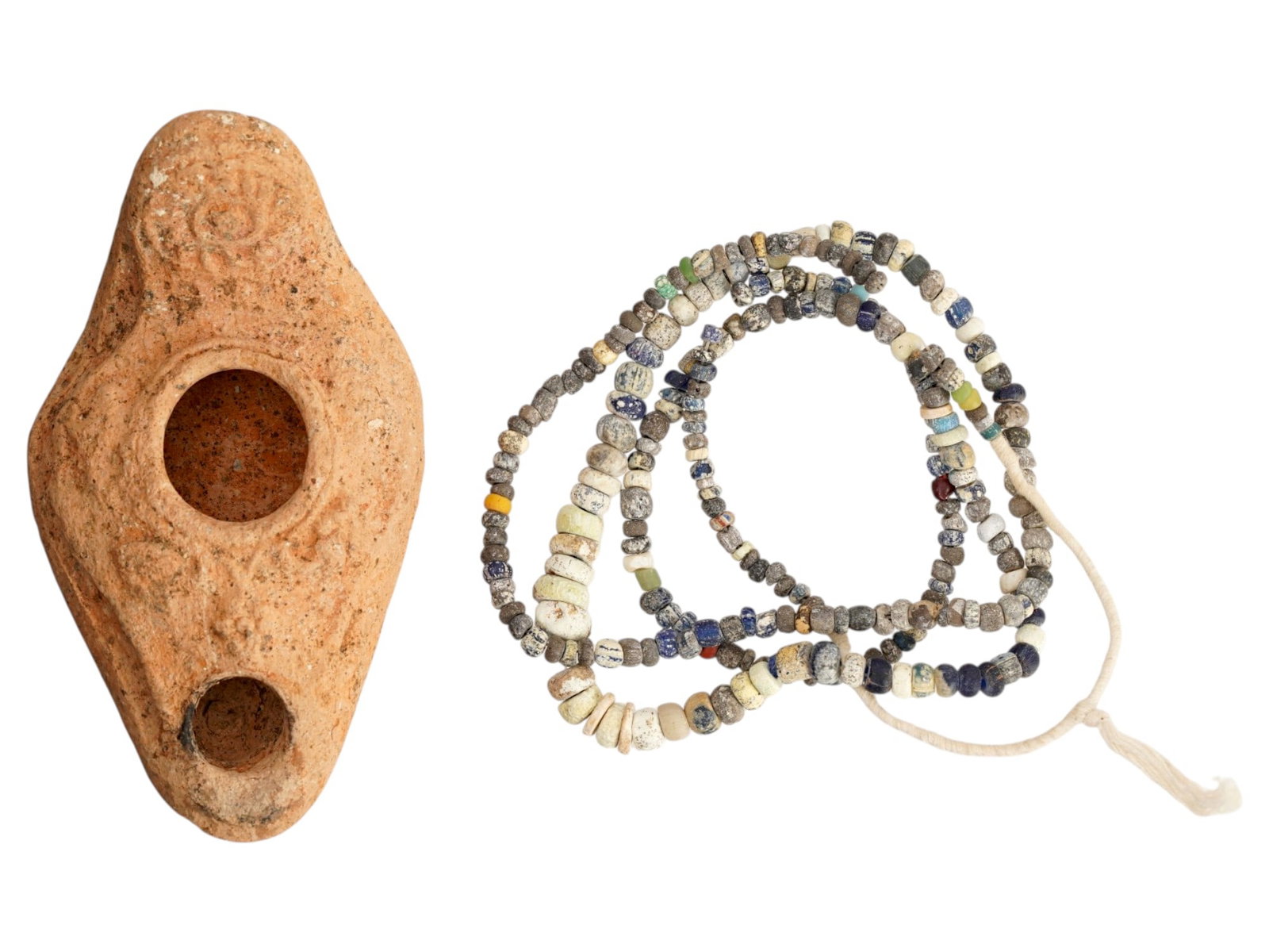 ANCIENT ROMAN TERACOTTA OIL LAMP AND GLASS NECKLACE: A lot of Ancient Roman artifacts. Imperial Rome era, ca. 100 to 300 AD. A glass beaded necklace. A terracotta oil lamp decorated with an eye on the handle and grapes on the sides. Historical Collectib