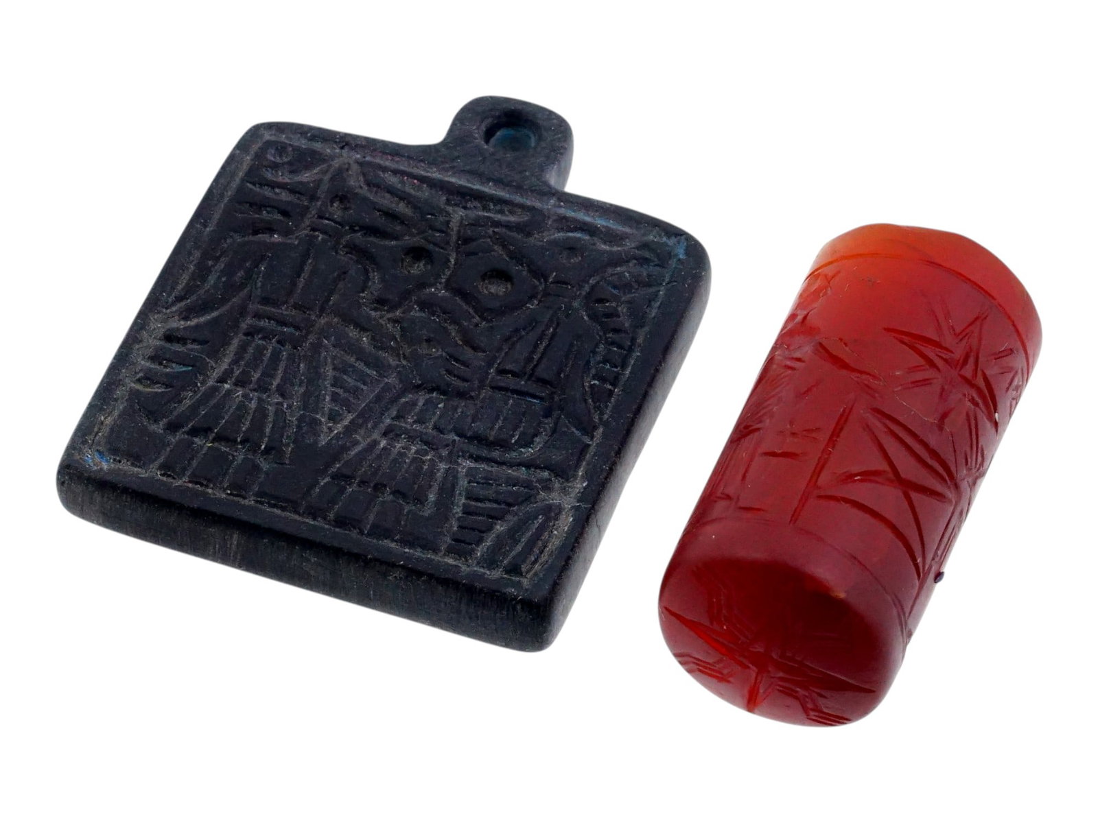 ANTIQUE GRAND TOUR CARVED STONE CYLINDER SEALS: A lot of two antique 19th-century hand-carved stone seals, reproductions of Sumerian stamps made for sale as a Grand Tour souvenir. The first pendant is cylindrical, while the second is square with a 