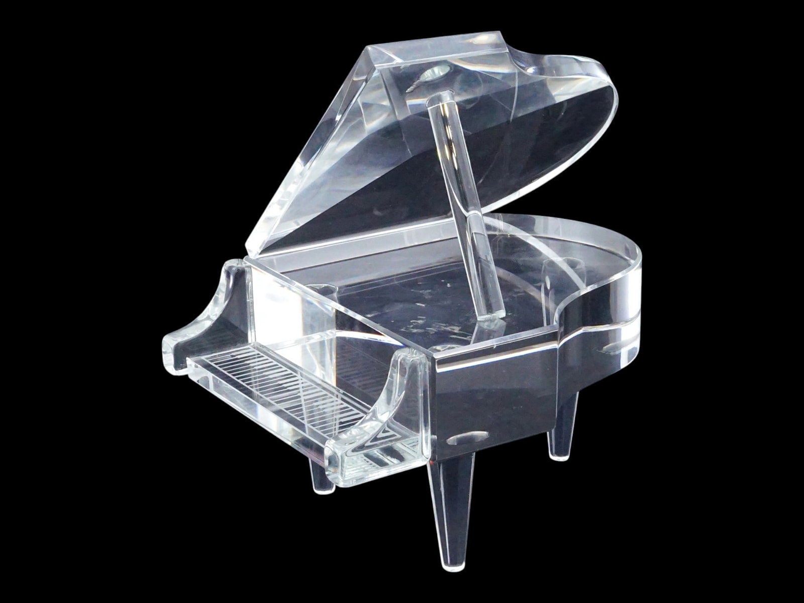 MINIATURE CLASSIC CLEAR GLASS GRAND PIANO FIGURINE: A miniature grand piano figurine is crafted from clear glass, featuring a classic grand piano silhouette supported by three tapered legs. The design includes a hinged lid that can be positioned open w