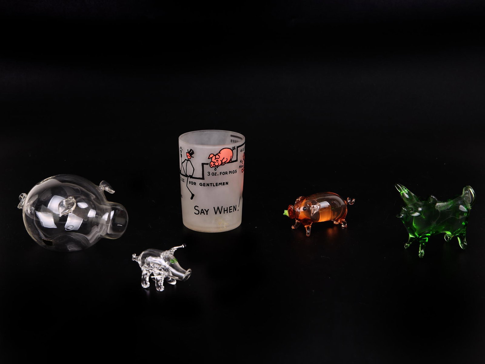 A LOT OF FIVE GLASS PIGS RELATED ITEMS FIGURINES: A lot of five pigs related glass items including four hand-blown figurines in various sizes, designs, and colors, the green piece is from Sweden; and an American frosted glass shot glass with a painte
