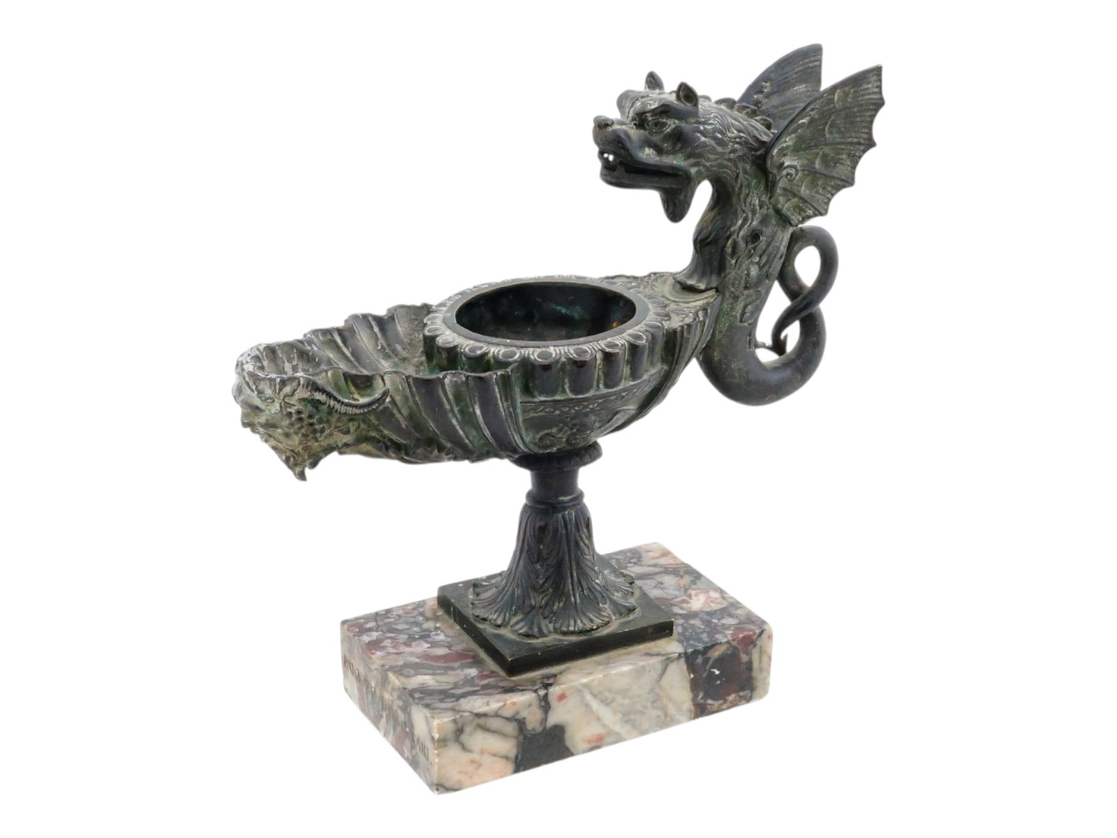 ANTIQUE GRAND TOUR BRONZE OIL LAMP ON MARBLE BASE: An antique Grand Tour bronze oil lamp or lucerne. The lamp is shaped like a bowl, decorated with relief patterns and the head of a fantastical creature probably a griffin on the spout. A distinctive d