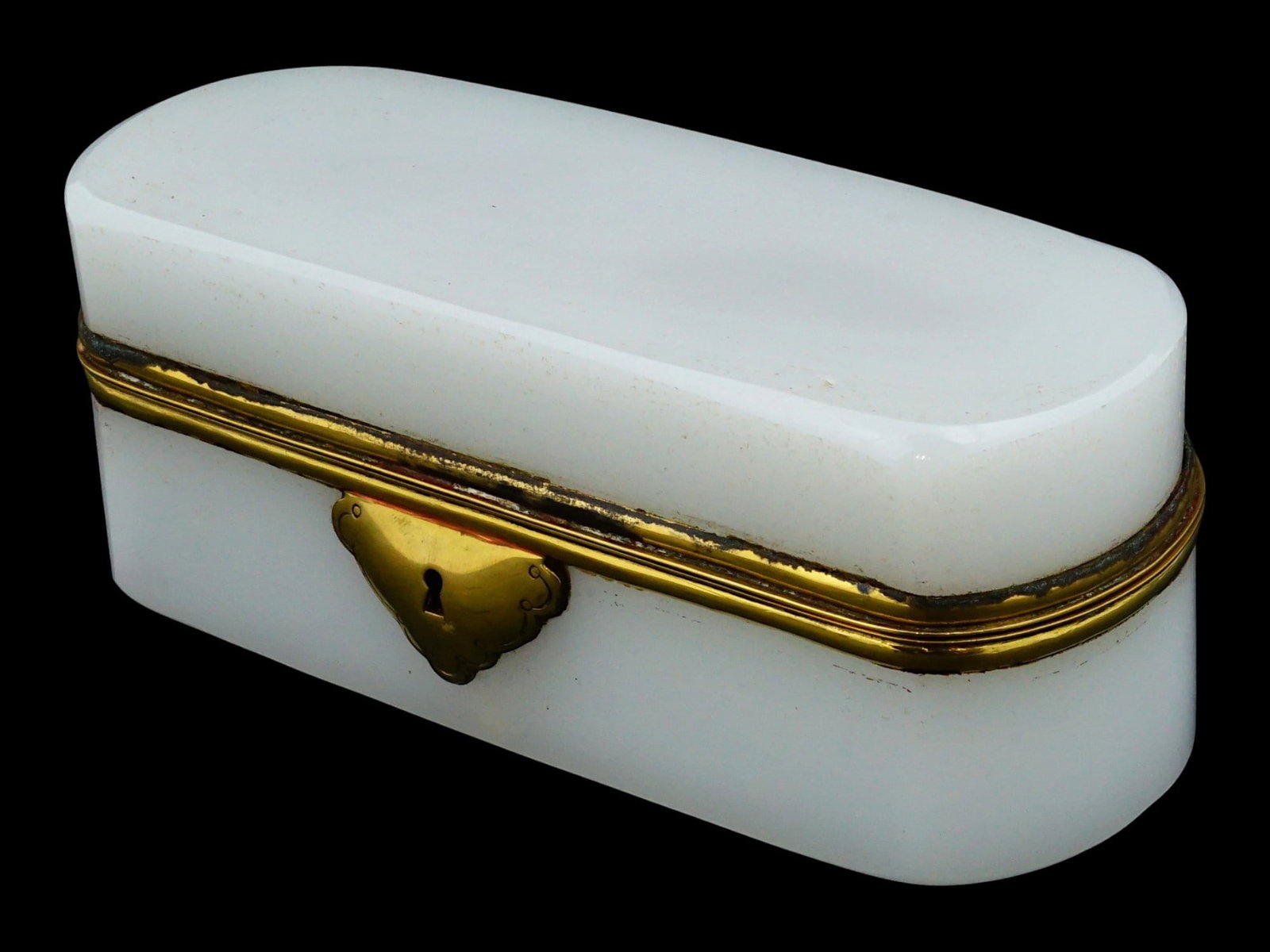 VINTAGE WHITE OPALINE AND BRASS MOUNTED JEWELRY BOX: A jewelry box, constructed from opaque white opaline glass, featuring an oblong silhouette with smooth, rounded edges and a polished surface. The box is secured with decorative brass mounts, including