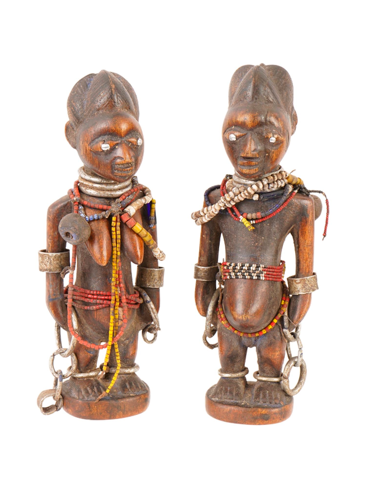 AFRICAN NIGERIA YORUBA ERE IBEJI WOODEN TWIN FIGURINES: A lot of two African Ere Ibeji sacred wooden twin figurines from the Yoruba culture of Nigeria. The pair of twins features an elaborate array of colorful necklaces and metal adornments, including chai