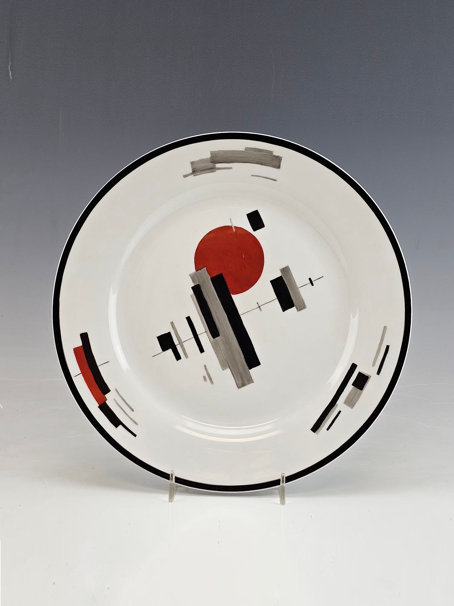 RUSSIAN PAINTED PORCELAIN PLATE AFTER NICOLAI SUETIN: A Russian Soviet era hand painted porcelain plate, Crossings in Black and Red, after Nicolai Suetin, Russian, Soviet era, 1897 to 1954. Marked and inscribed, on the backside. Nikolai Suetin was a Russ