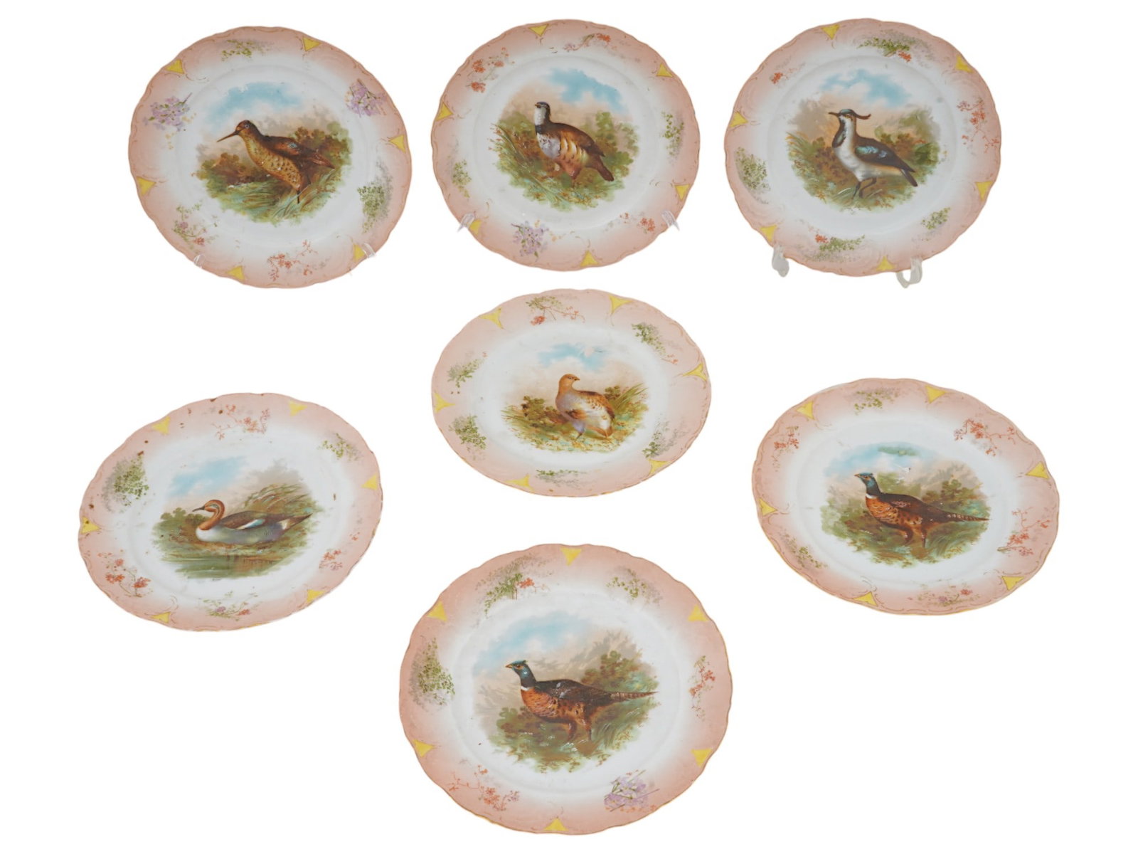 COLLECTION OF 7 PORCELAIN PLATES WITH BIRDS: A collection of seven porcelain plates, each featuring a hand-painted depiction of a different game bird. The plates have a slightly scalloped or wavy edge and a decorative border that is predominantl