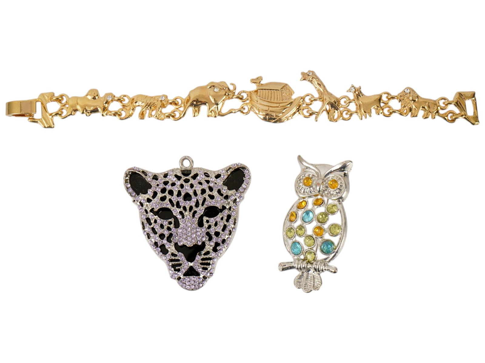 COLLECTION OF VINTAGE COSTUME JEWELRY PIECES: A collection of costume jewelry, featuring a mix of vintage pieces. Includes a Noahs Ark link bracelet with animal motifs, a leopard-head pendant set with contrasting crystals, and an owl brooch adorn