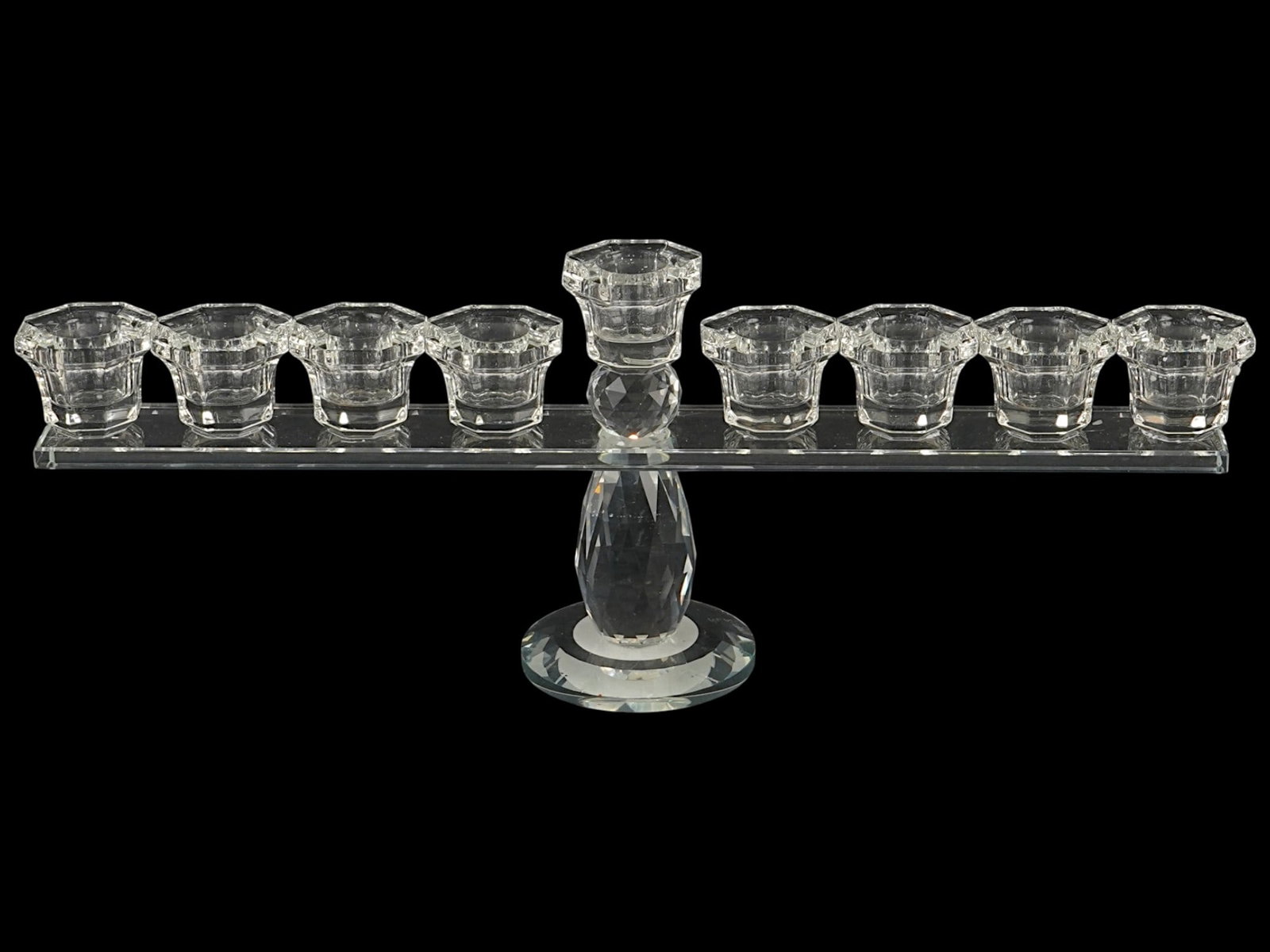 CONTEMPORARY HANUKKAH MENORAH CANDLEHOLDER: A contemporary Hanukkah menorah candleholder, made of faceted lead crystal featuring a brilliant, light-refracting surface. The design comprises a horizontal bar supporting eight candle cups, centered