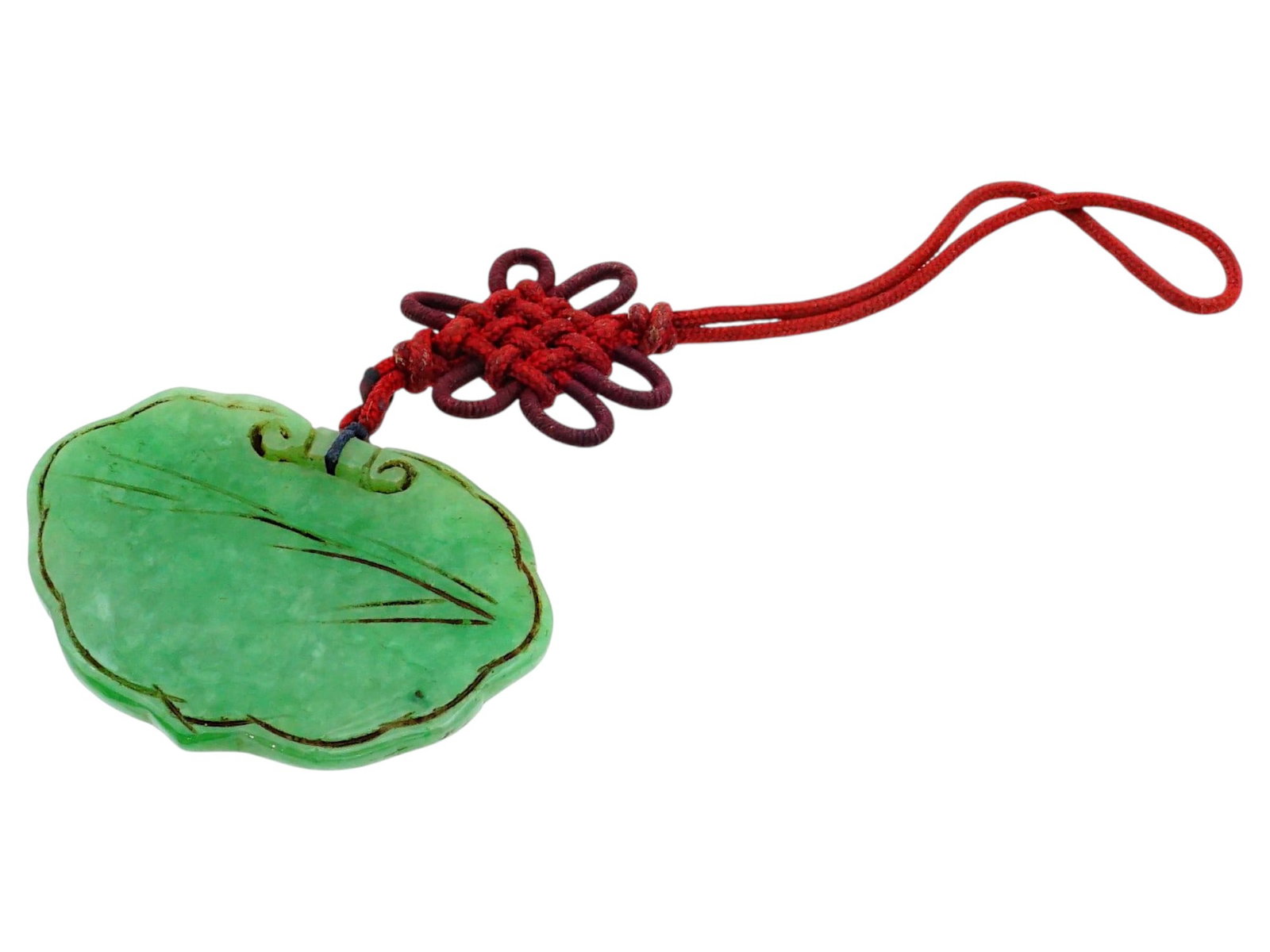 CHINESE CARVED GREEN JADE PENDANT ON RED CORD: A Chinese carved green jade pendant in the traditional ruyi-head form, a classic motif symbolizing longevity and the fulfillment of wishes. The medallion features low-relief scrolling motifs on the su