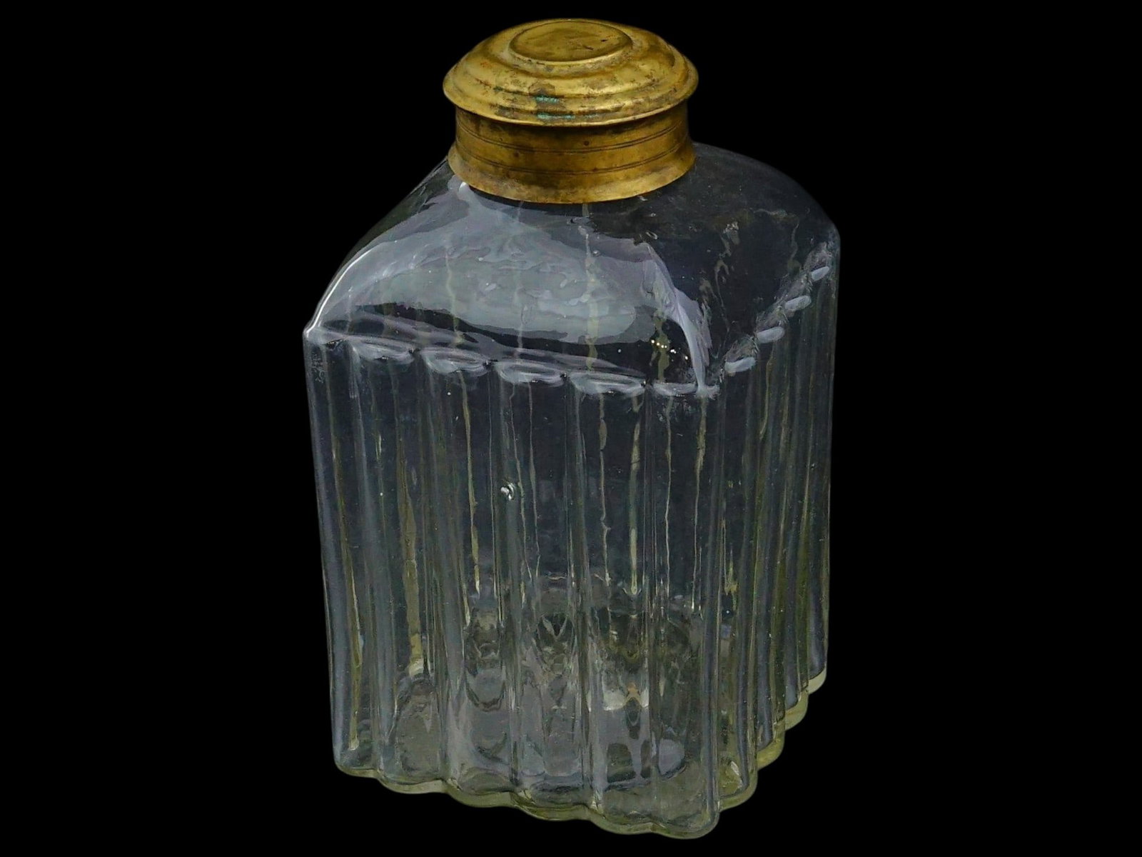 ANTIQUE RIBBED DESIGN GLASS TEA CADDY WITH BRASS LID: An antique glass tea caddy with a relief body.T he body of the tea caddy is made of thick walled transparent glass with a distinctive vertical ribbed or pleated pattern. The neck is fitted with a scre