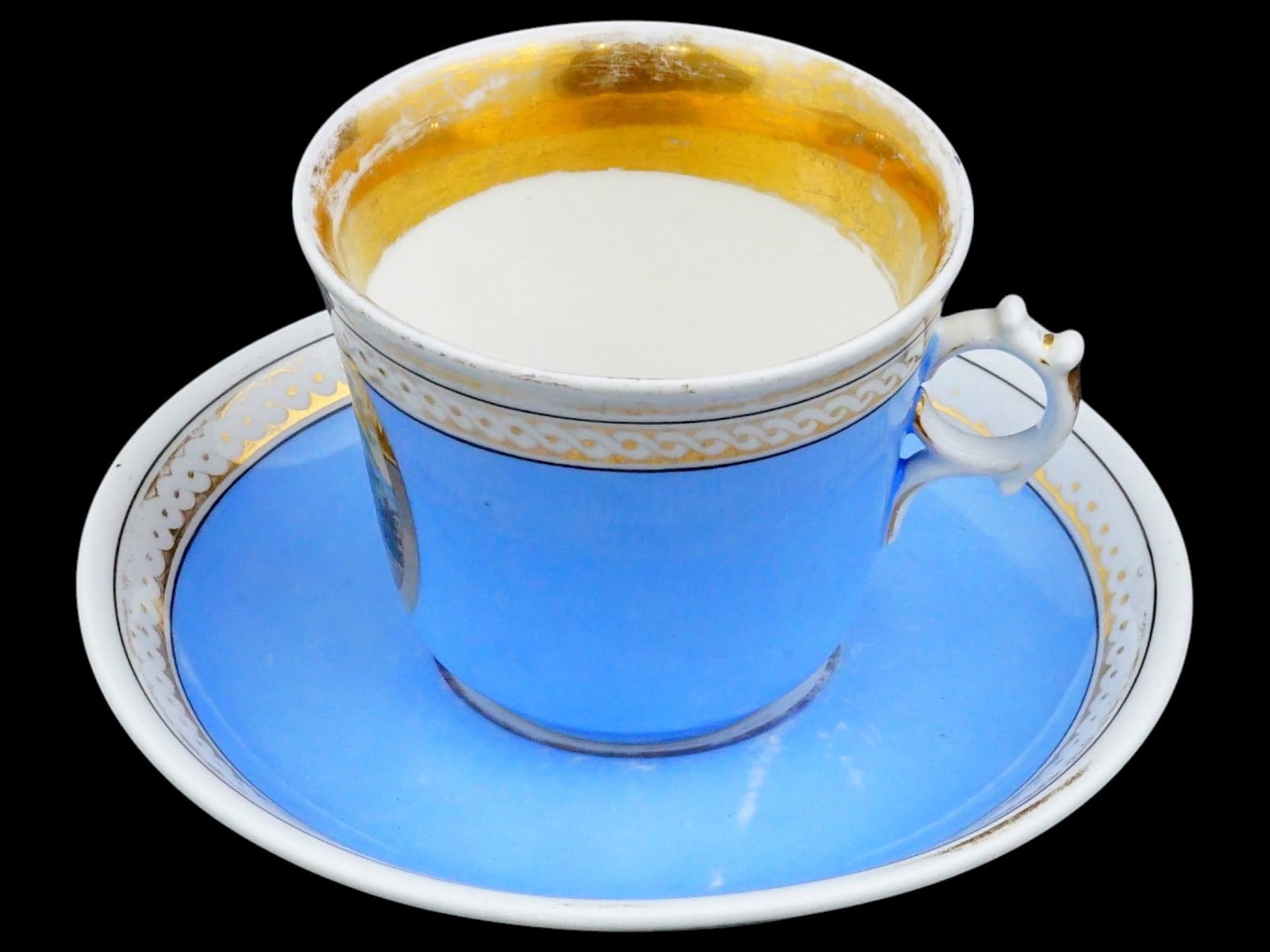ANTIQUE PORCELAIN TEA CUP SET BY CARL TIELS?H ALTWASSER: An antique 19th-century porcelain tea cup and saucer set by Carl Tiels?h Altwasser, Silesia. On the cup, against a blue background, is an oval medallion with a gold edge depicting the god of medicine,