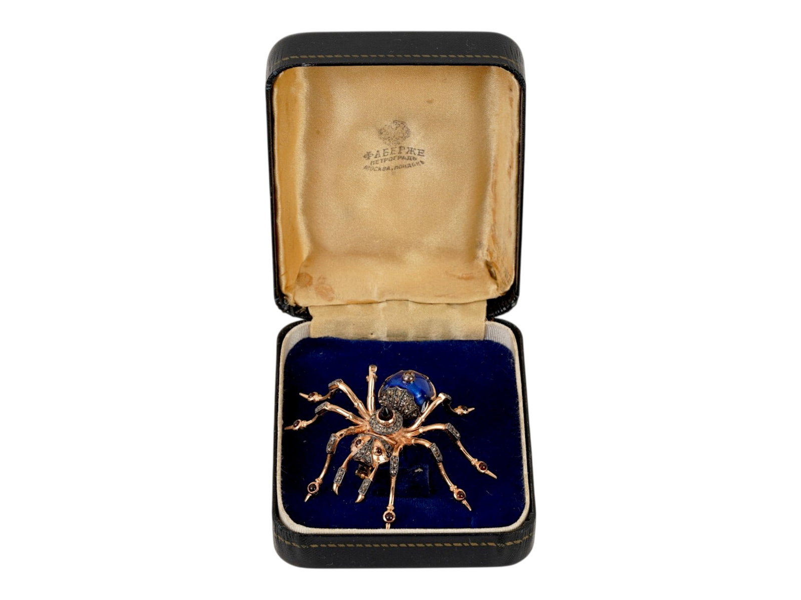 RUSSIAN GOLD ENAMEL DIAMOND AND RUBY SPIDER BROOCH: A Russian gold pin brooch representing a spider. The piece is garnished with cobalt blue guilloche enamel, ruby cabochons, and diamonds. Hallmark of 56 gold standard and makers mark are on the pin.