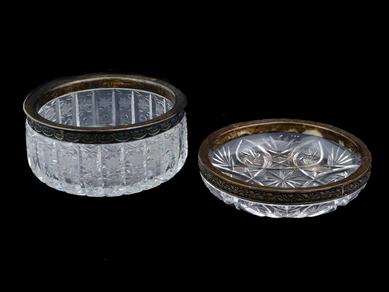 TWO RUSSIAN CRYSTAL CUT GLASS AND SILVER MOUNTED BOWLS: A lot of two Russian cut glass bowls, each featuring distinct decorative motifs and chased silver mounts. The first bowl features a classic geometric pattern with starbursts and interlocking curved