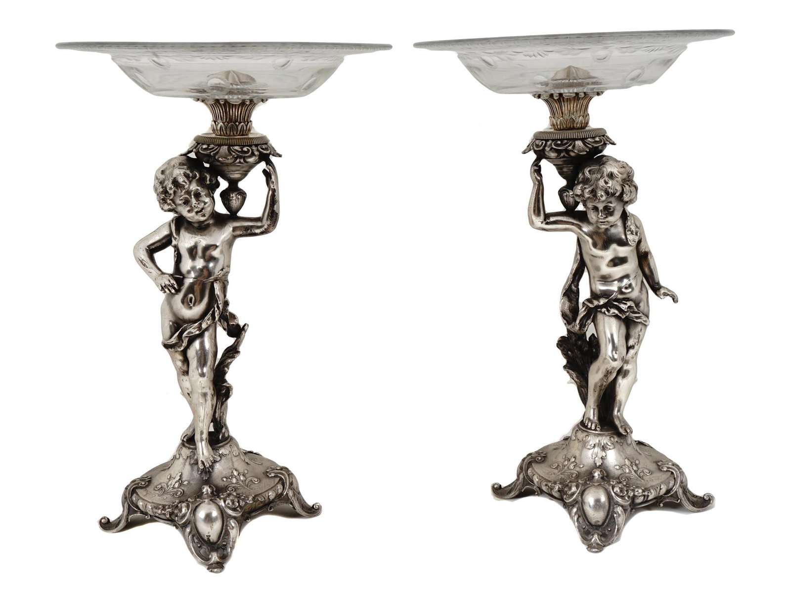 PAIR OF GLASS SILVER PLATED CENTER PIECES VASES: A pair of vintage cut glass and silver plated center pieces or vases. The bodies of the vases are made in the shape of a cherub holding a bowl and adorned with an embossed foliage pattern. The glass b
