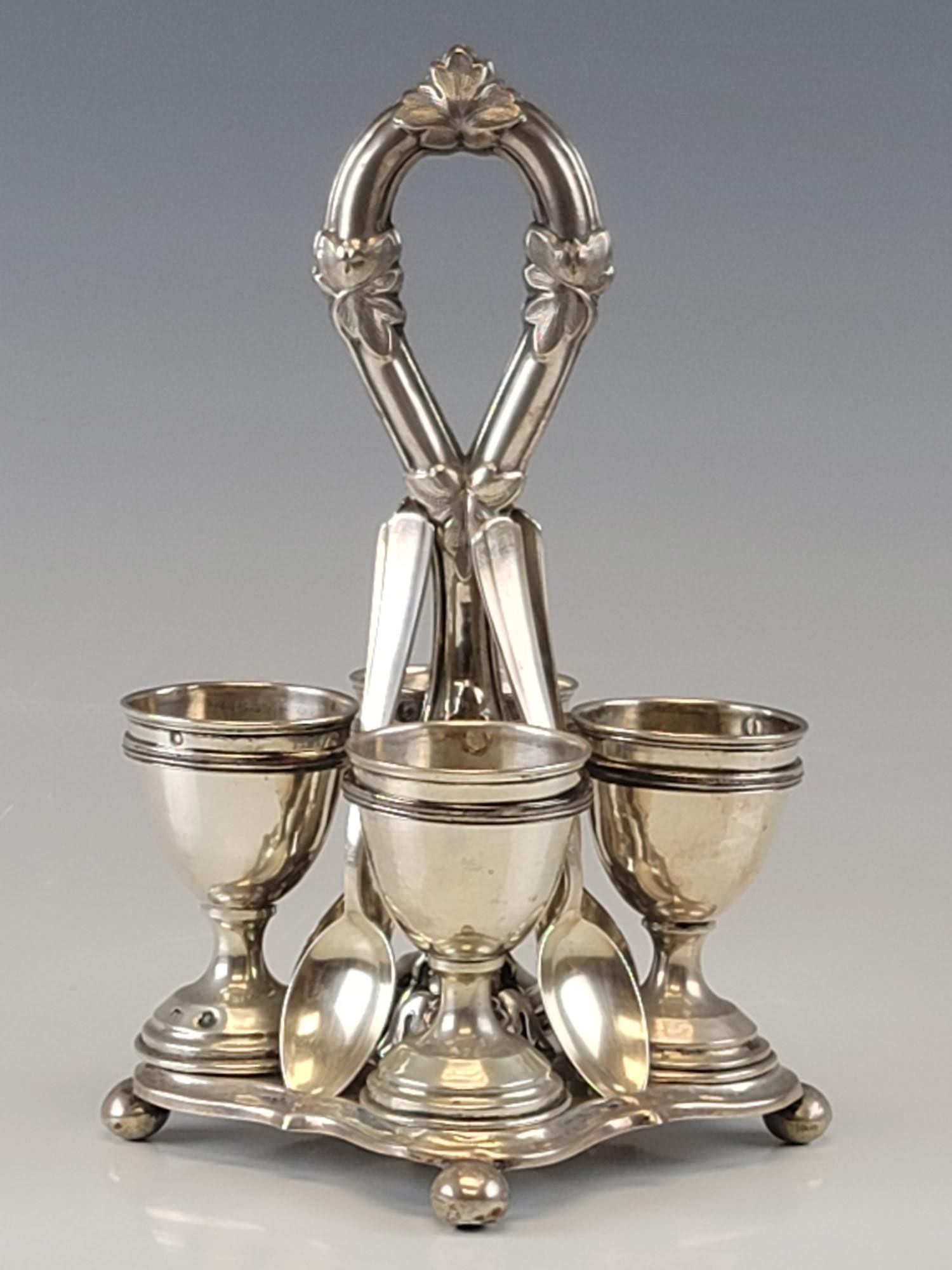 19C ANTIQUE AUSTRIAN SILVER EGG SERVER CUPS SPOONS: An antique 19th century Austrian silver egg server set comprising a stand, four cups, and four spoons. The stand is raised on four bun feet with a diamond shaped base and a loop-style handle entwined