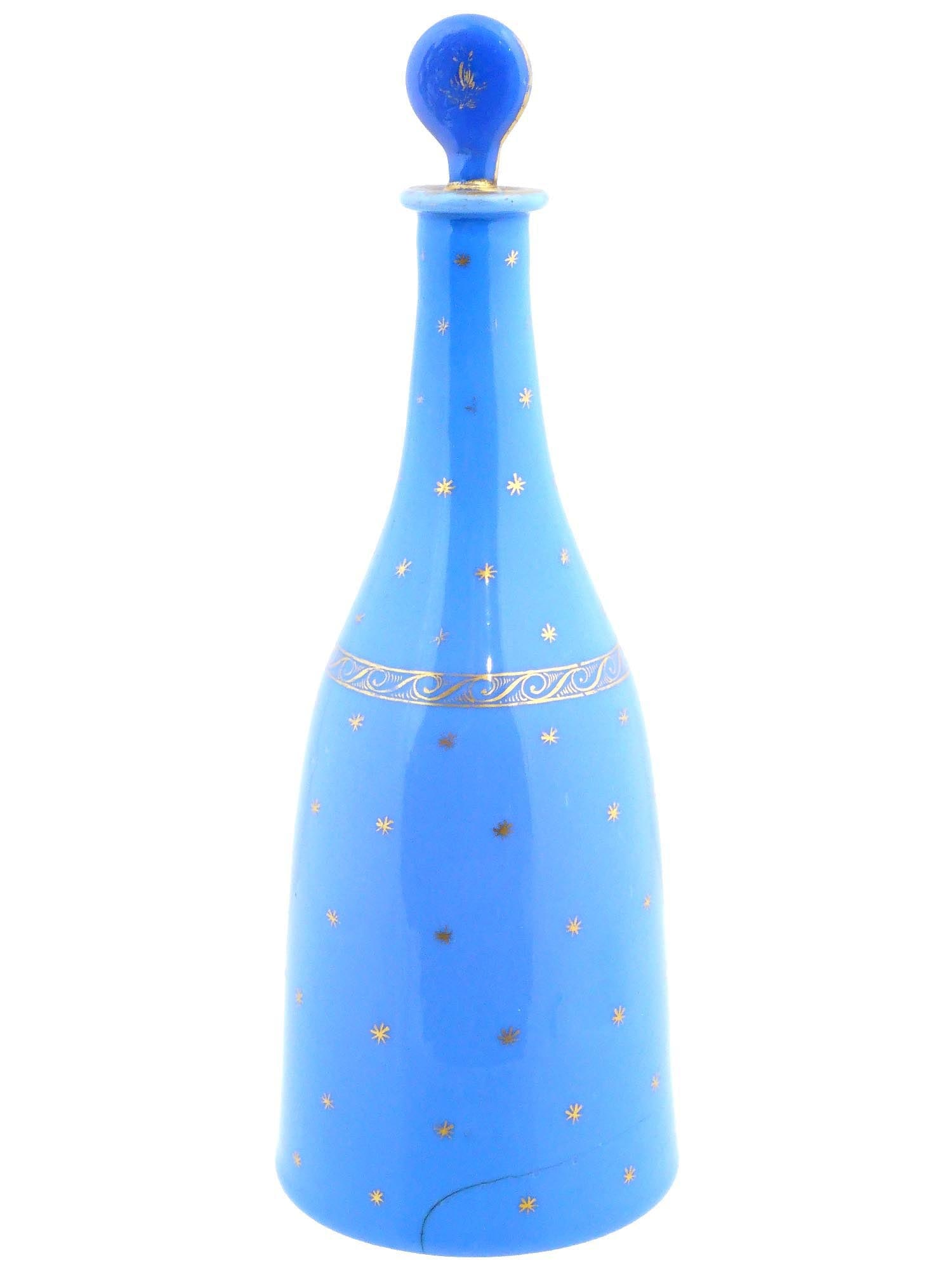 ANTIQUE FRENCH BLUE OPALINE GLASS VANITY BOTTLE: An antique French blue opaline glass vanity bottle with a stopper. The piece features a blue color, complemented by intricately designed olden accents. Adorned with delicate gold leaf patterns and sta