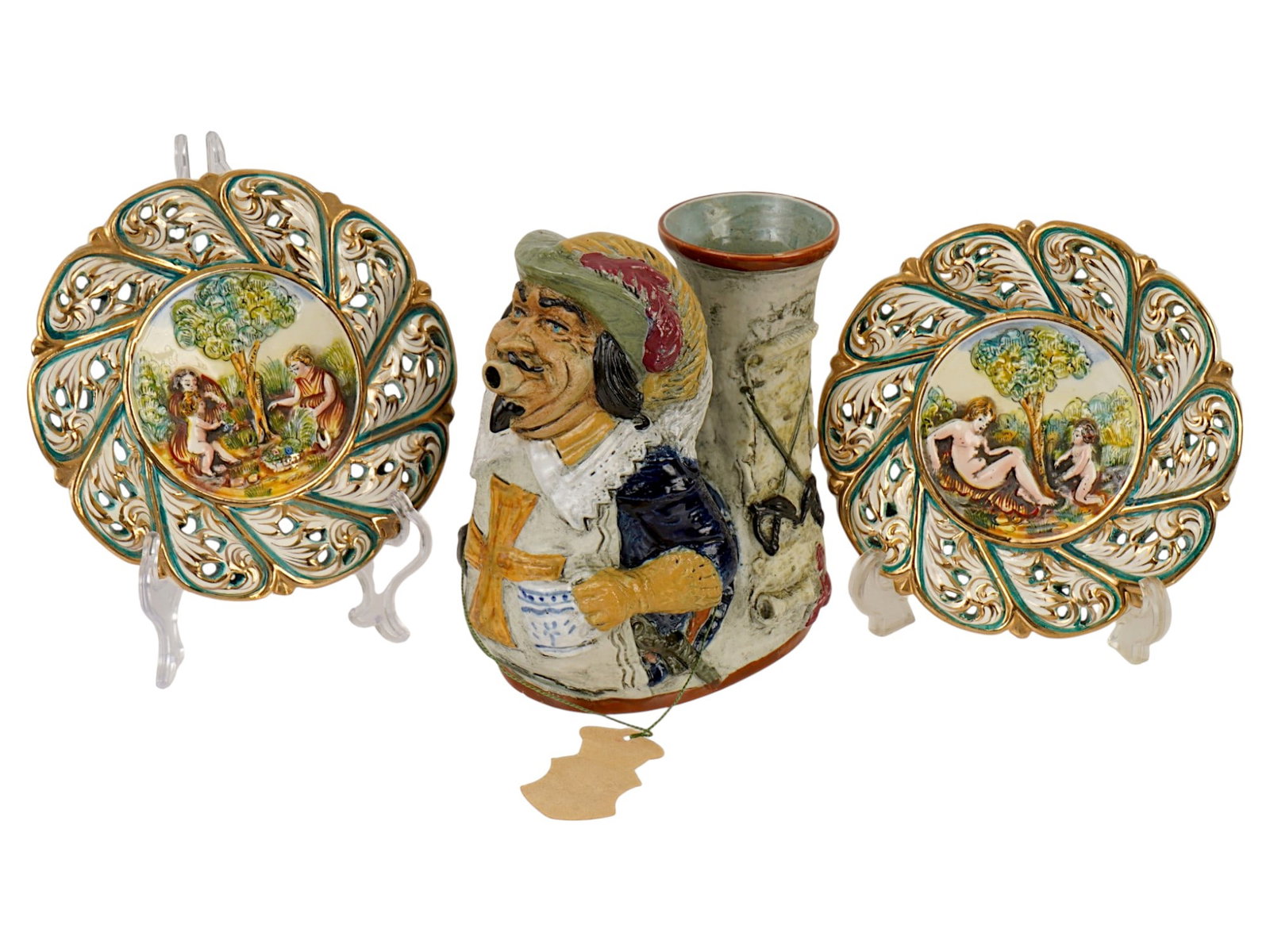 VTG ITALIAN CERAMIC PLATES AND CAPODIMONTE PITCHER: A pair of vintage Italian hand painted ceramic plates and a Cavalier musketeer decanter pitcher, produced by Capodimonte in the 1960s. The pair of round plates with an openwork petal design, painted