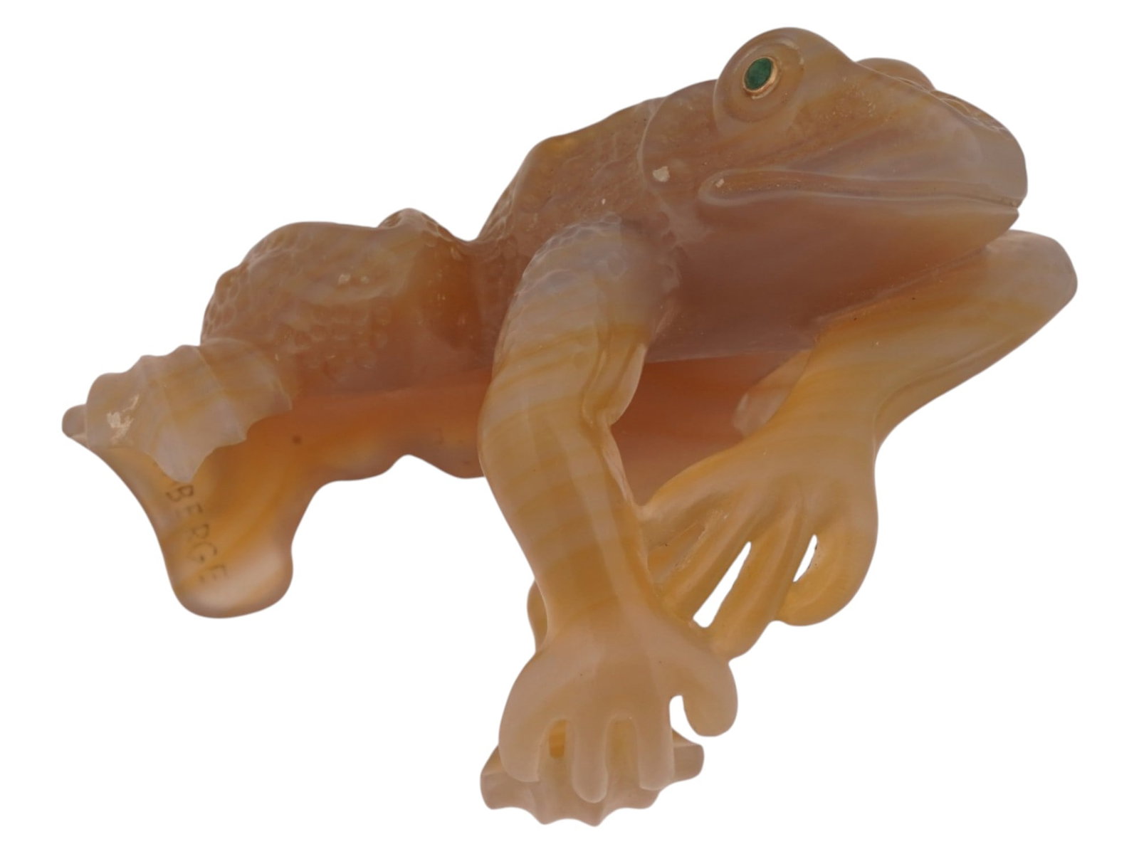 RUSSIAN CARVED AGATE FROG NAPKIN RING W EMERALD EYES: A Russian carved honey agate napkin ring in the shape of the frog. The creatures anatomy is detailed with a textured dorsal surface, while its elongated limbs curve beneath the body to create a