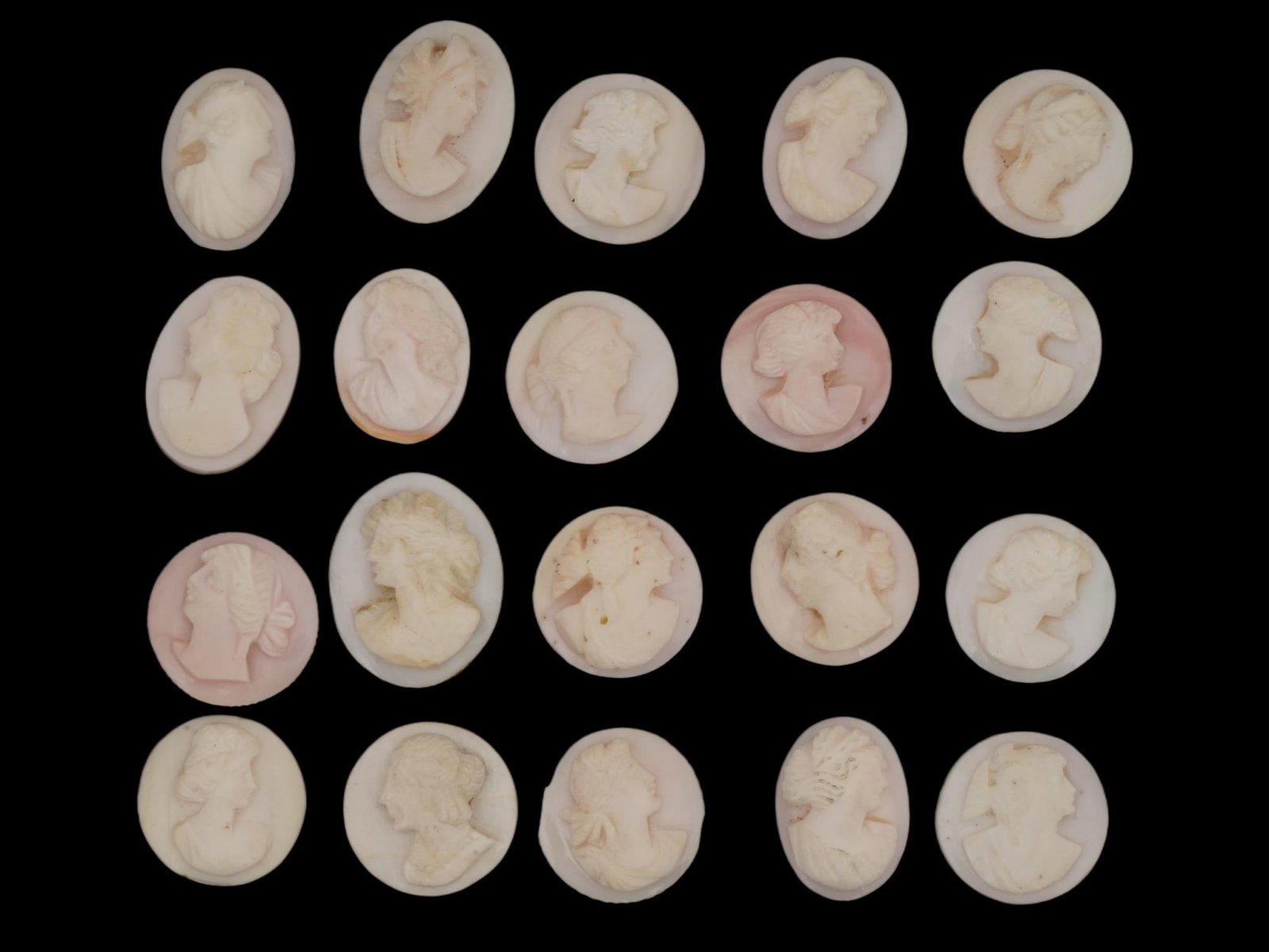 COLLECTION OF FEMALE PORTRAIT CARVED CORAL CAMEOS: A collection of hand carved pink coral cameos. A total of 20 items. Each piece depicts a female profile portrait rendered in high relief. Round and oval shape. Collectible Jewelry And Glyptic Art, Scu