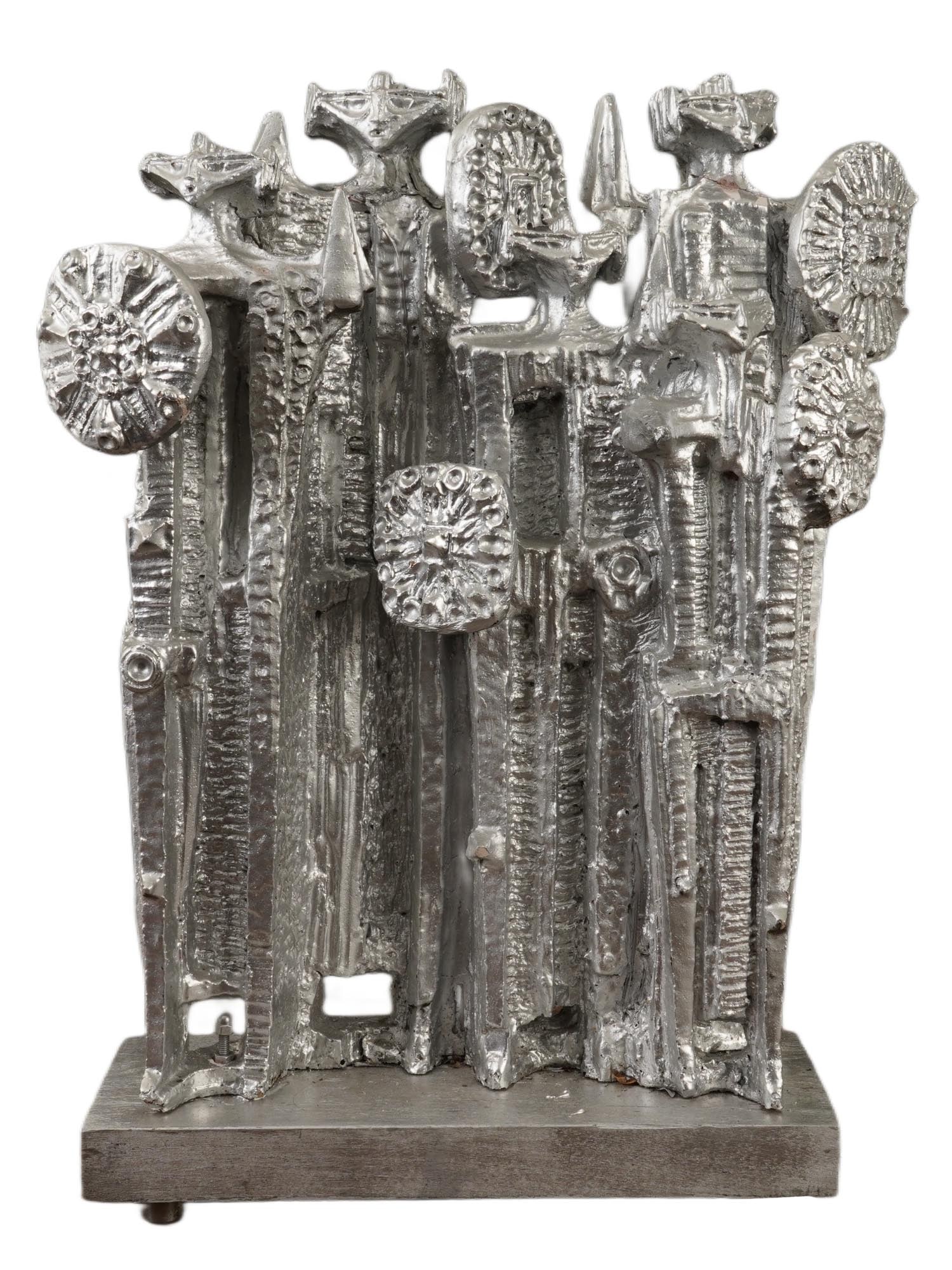 ABSTRACT ALIENS CERAMIC SILVER COLORED SCULPTURE: An abstract ceramic silver-colored sculpture mounted on a wooden base featuring likely aliens. The piece consists of multiple vertical, pillar-like forms of varying heights, grouped tightly together t