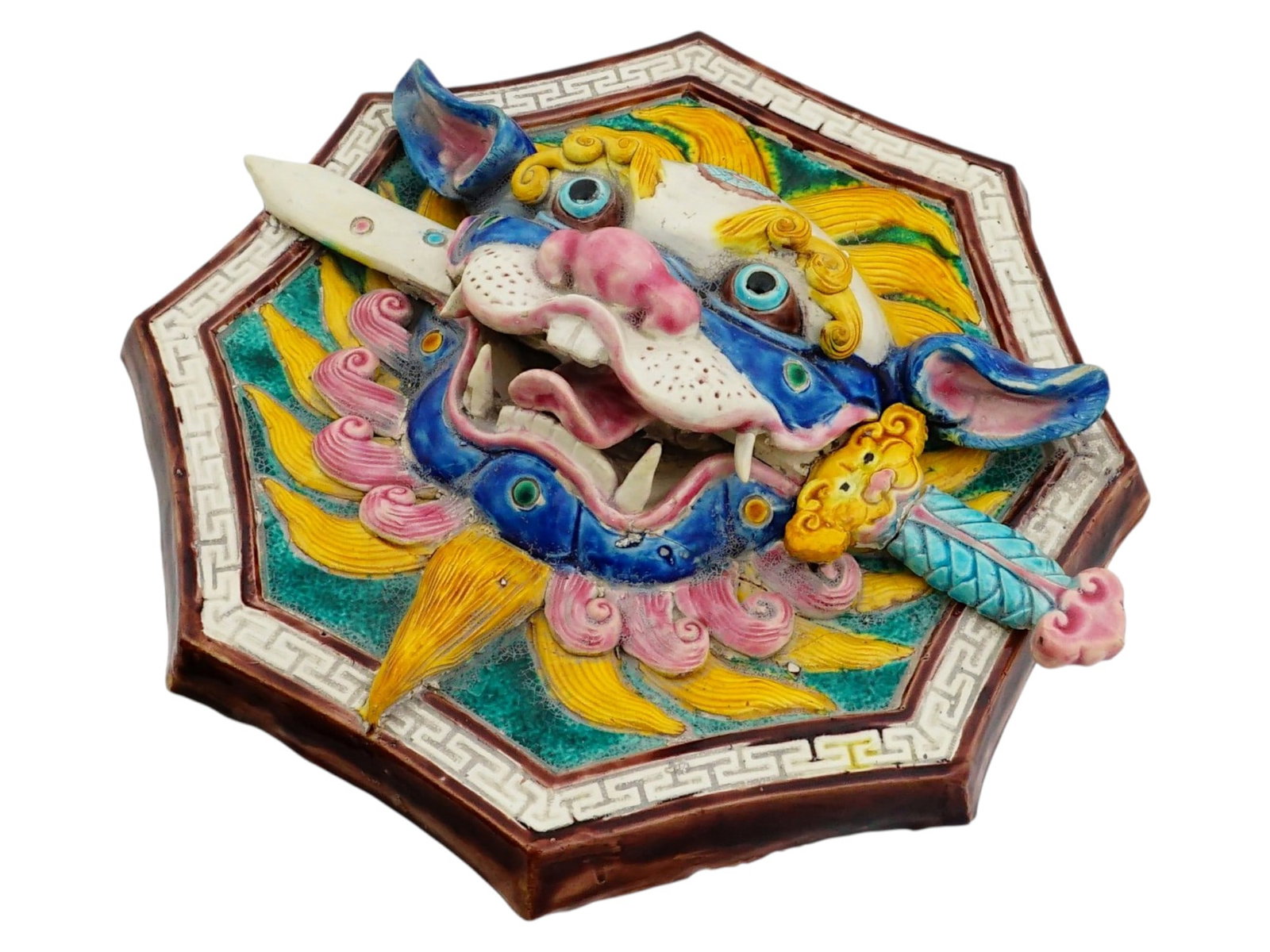 CHINESE OCTAGONAL GLAZED CERAMIC WALL PLAQUE: A Chinese octagonal glazed ceramic wall plaque, featuring a high-relief depiction of a Shishi or Lion Dog biting a ceremonial sword. The central figure is rendered in vibrant shades of cobalt blue, ye