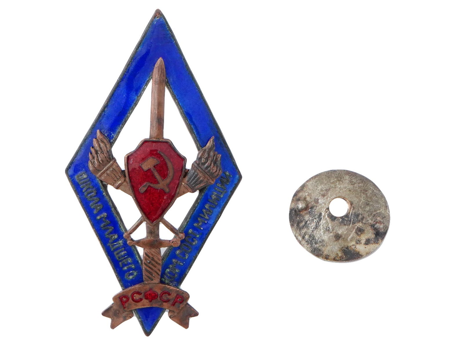 RUSSIAN SOVIET BRONZE ENAMEL BADGE JUNIOR POLICE SCHOOL: A Russian Soviet bronze enamel badge of the RSFSR Junior Police School. Features a central red shield adorned with a hammer and sickle. Behind the shield are two crossed torches and a sword. At the bo