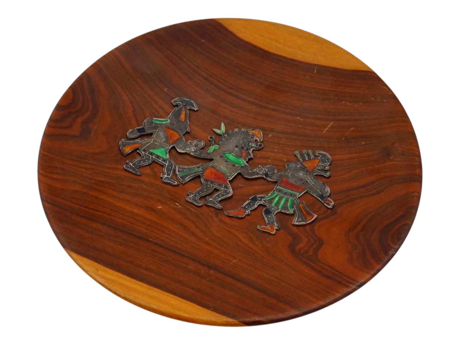 MEXICAN FIGURES SILVER ENAMEL INLAID WOODEN PLATE: A circular decorative charger crafted from a dark, polished wood and features a central figurative composition executed in silver toned metal inlay and polychrome enamel. The scene depicts three styli