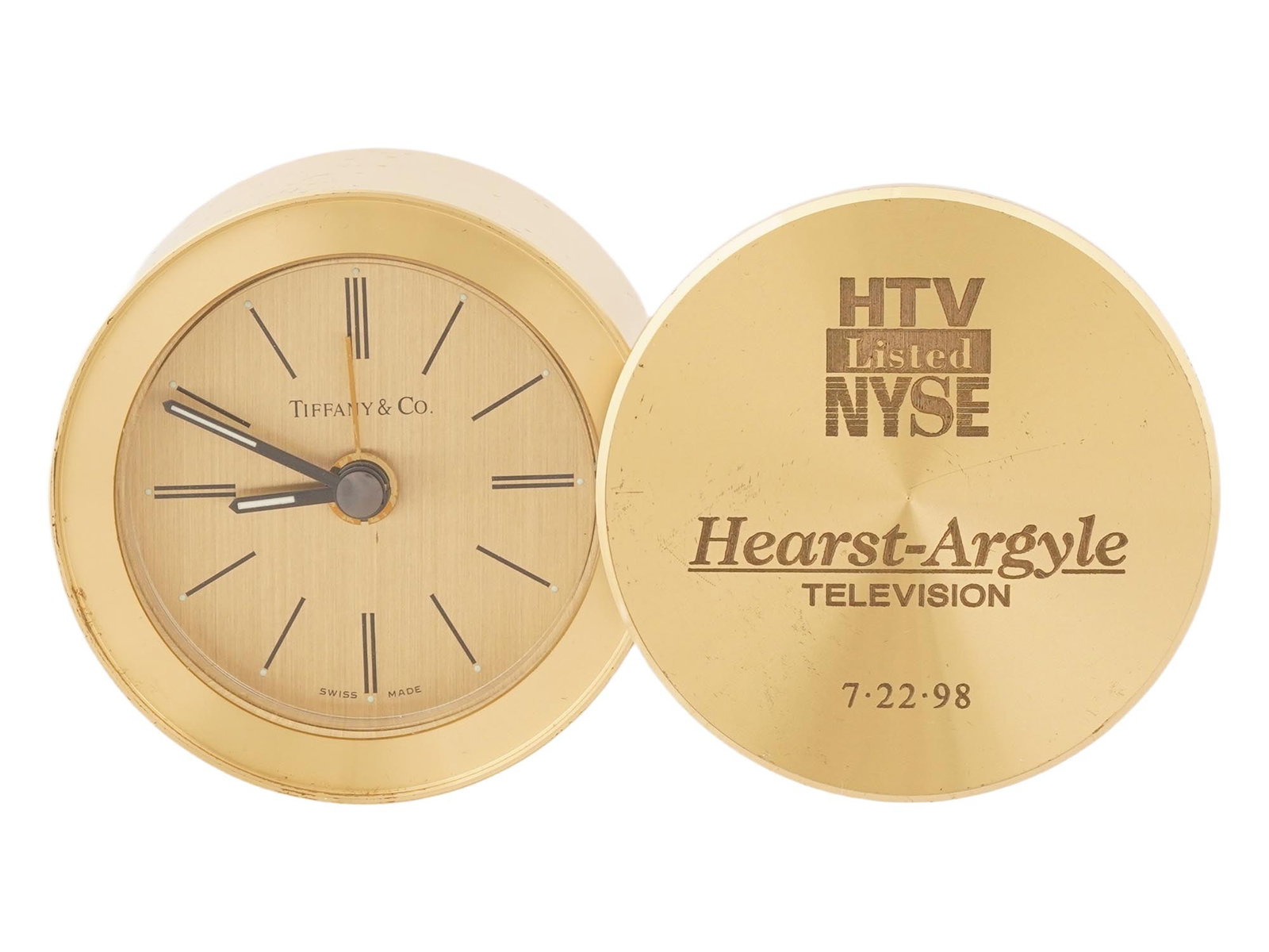SWISS MADE TIFFANY AND CO GILT BRASS TRAVEL CLOCK: A vintage Swiss made Tiffany and Co. gilt brass travel alarm clock. The quartz clock is designed as a cylindrical case with a lid. The dial is round, without numerals, and is marked Tiffany and Co.,