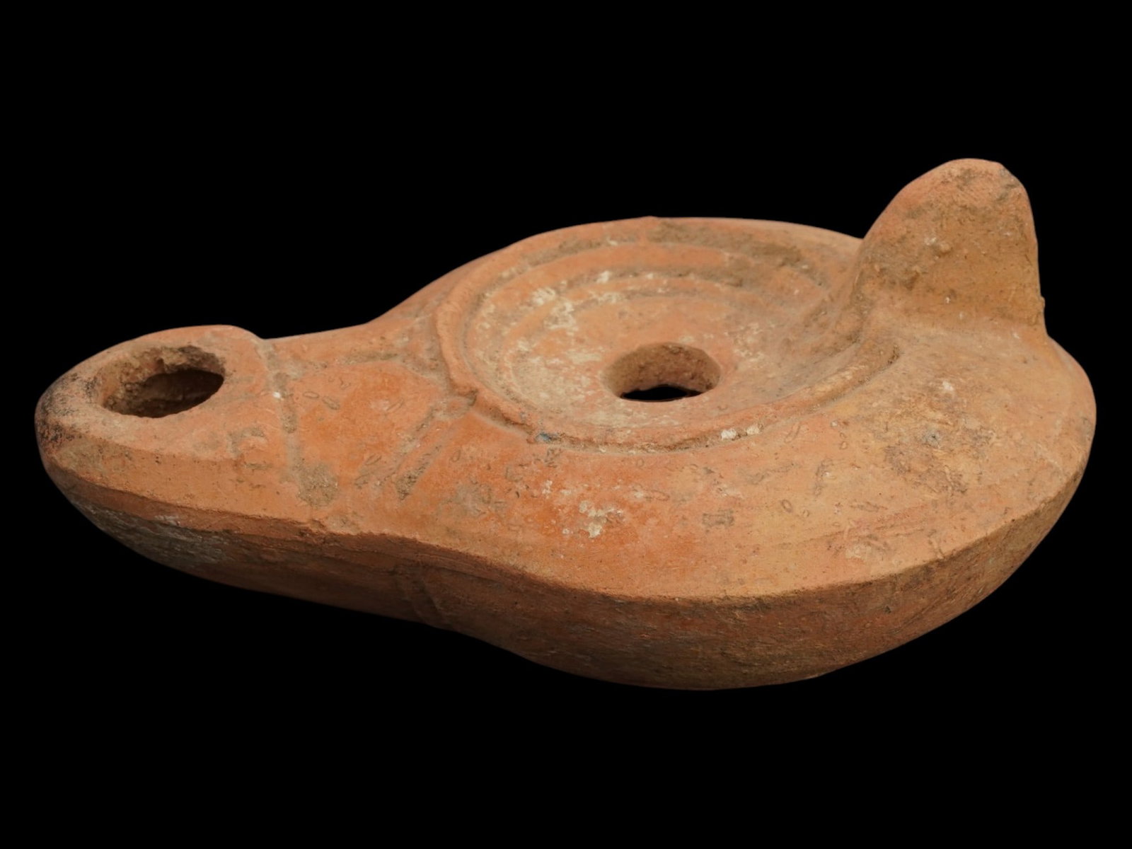 ANCIENT ROMAN TERRACOTTA OIL LAMP 100 TO 300 AD: An ancient Roman terracotta pottery oil lamp. The body of the lamp is adorned with geometric ornaments and an inscription on the bottom. The lamp features a raised circle nozzle top and a raised handl