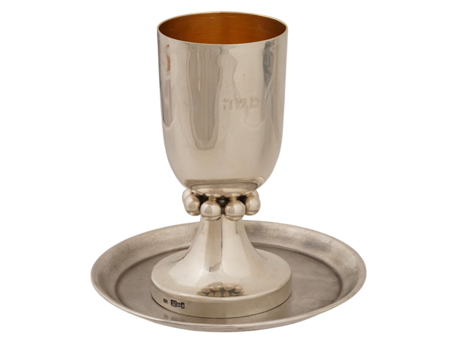 RUSSIAN SILVER JUDAICA CUP AND SAUCER WITH INSCRIPTION: A Russian silver Judaica cup and saucer set featuring a hand-engraved Hebrew inscription on the front of the cup. The design is highlighted by a distinctive collar of silver spheres around the stem. H