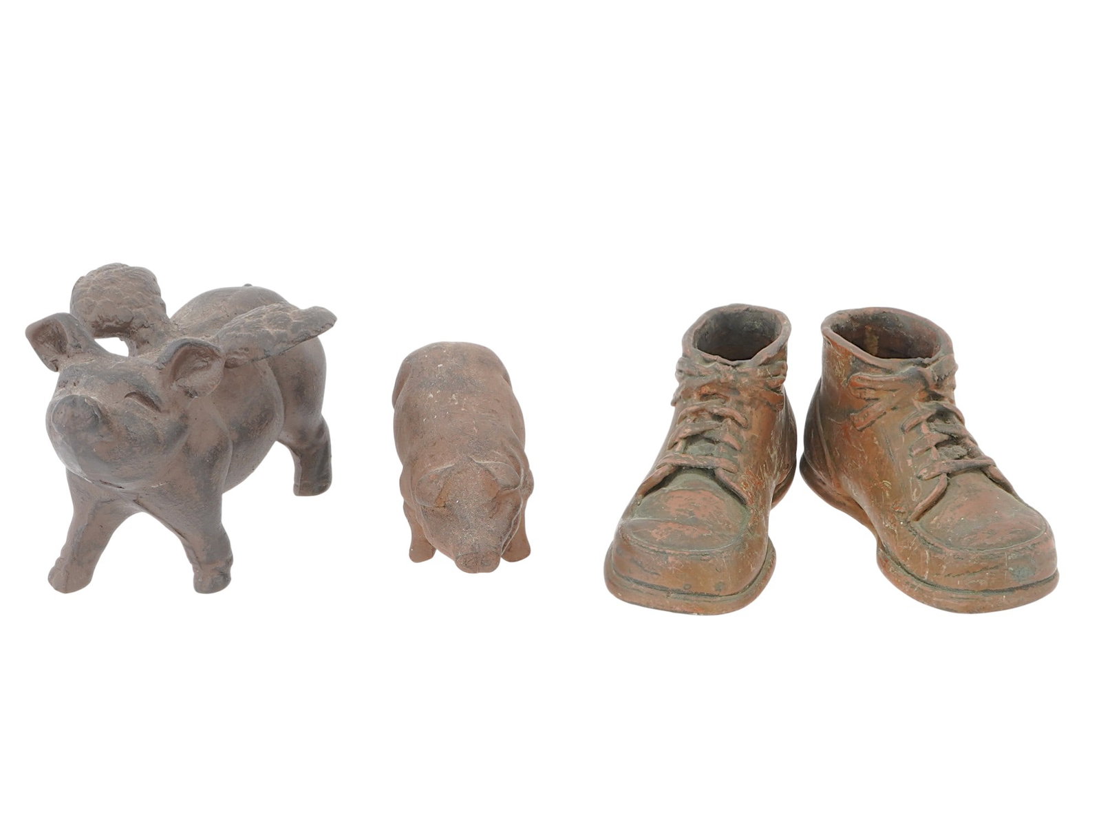 CAST IRON PIGS AND COPPER SHOES SCULPTURES: A lot of four cast iron and copper sculptures. Including two cast Iron pigs: The first pig is larger and has a pair of wings, attached to its back. The second pig is smaller, without wings. A pair of 
