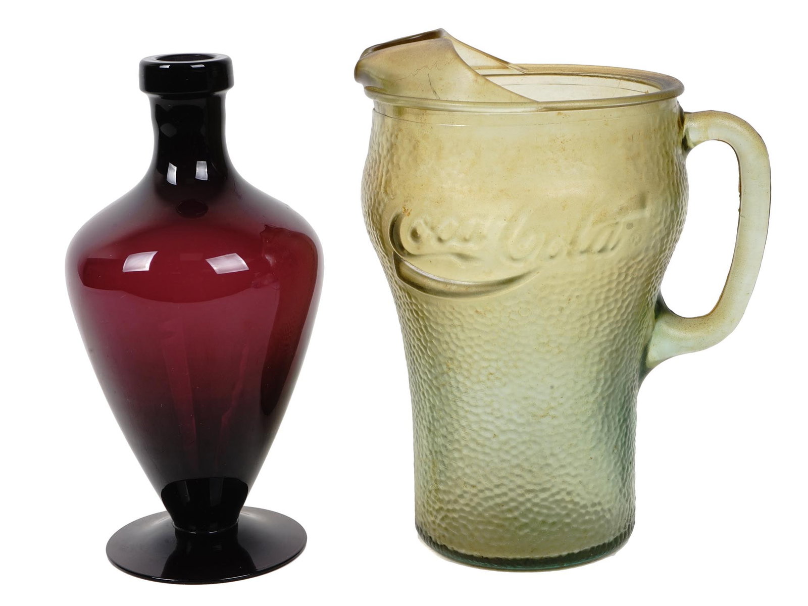VINTAGE GREEN GLASS PITCHER AND RED GLASS VASE: A vintage Coca Cola pebbled green glass pitcher. Circa the 1980s. A vintage tulip dark red glass vase in the form of a bottle on a circle base with a long thin neck. Vintage Vases And Glassware Collec