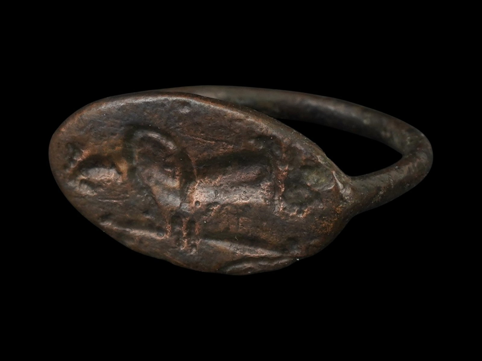 ANCIENT GRECO ROMAN BRONZE SIGNET RING 300 TO 100 BC: An ancient Greco Roman bronze signet ring features a prominent, flattened oval bezel. Circa 300 to 100 BC. The intaglio decoration depicts a human figure. The bezel is supported by a simple, rounded h