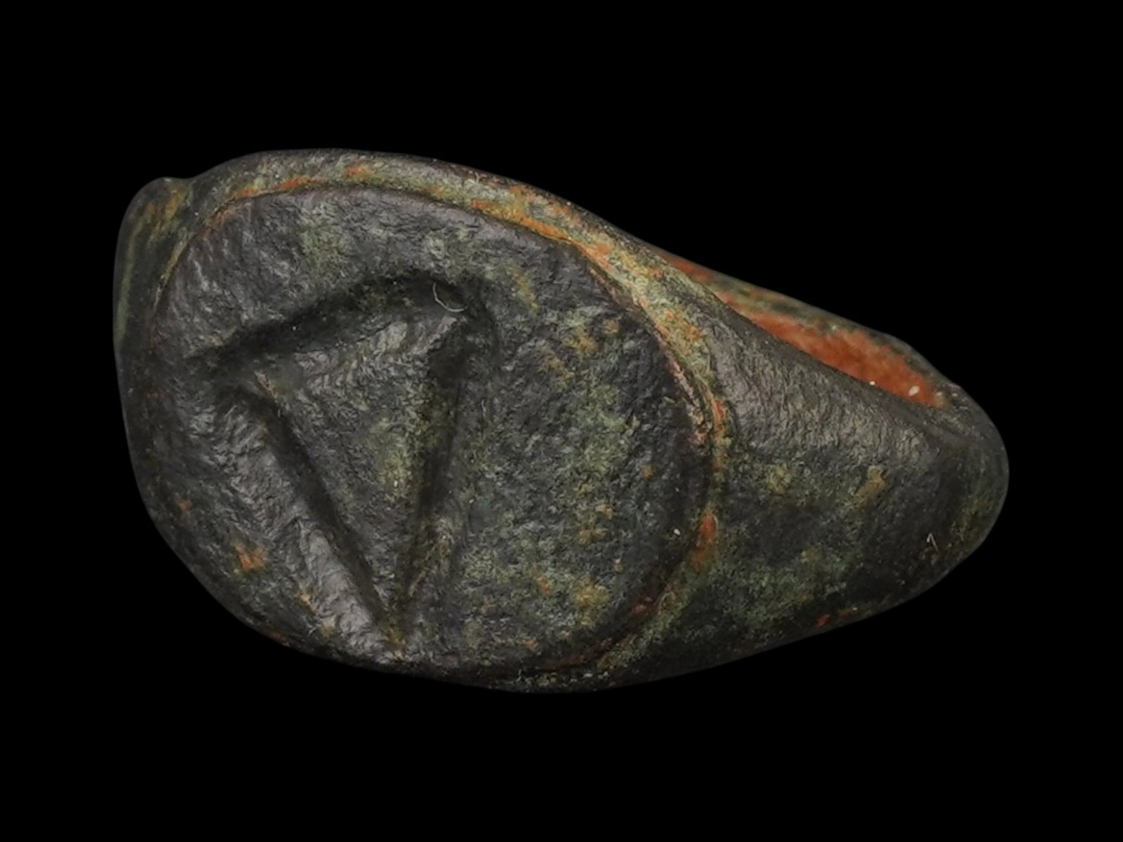 ANCIENT GRECO ROMAN BRONZE SIGNET RING 300 TO 100 BC: An ancient Greco Roman bronze signet ring features a prominent, flattened oval bezel. Circa 300 to 100 BC. The intaglio decoration depicts a triangle. The bezel is supported by a simple, rounded hoop 