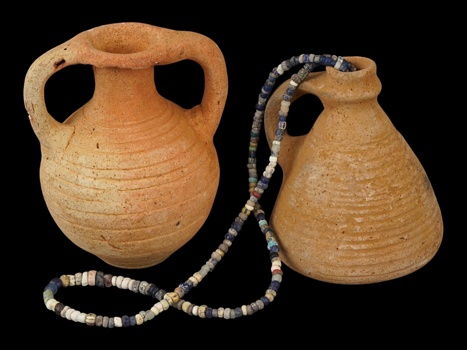 ANCIENT ROMAN TERRACOTTA PITCHERS GLASS BEAD NECKLACE: A group of two Roman Imperial terracotta pottery vessels and a glass bead necklace. Circa: 100 to 300 AD. The first vessel is a two handled amphoriskos with a globular body, while the second is a sing