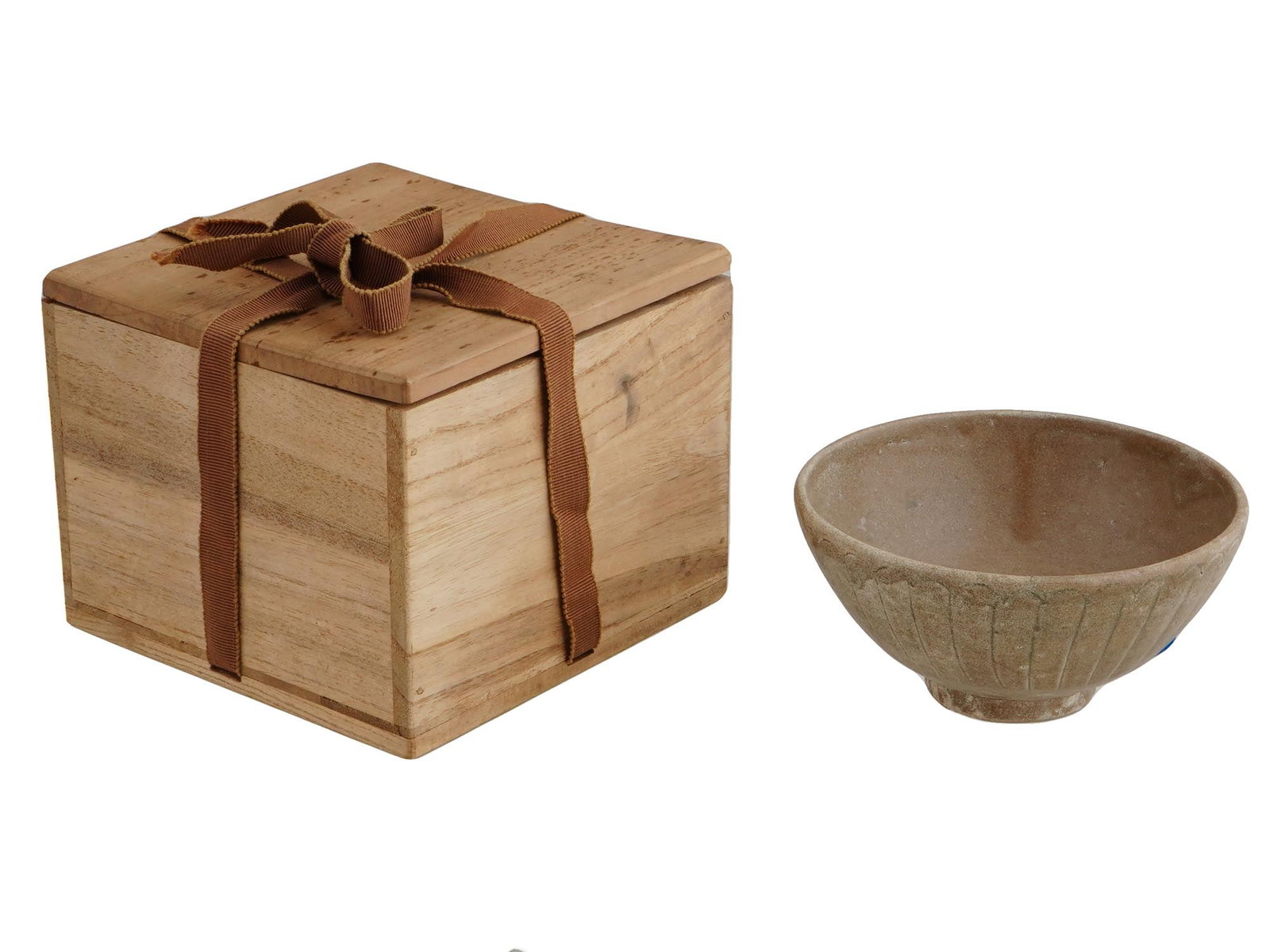 JAPANESE ENGRAVED POTTERY TEA BOWL WITH WOOD BOX: A Japanese footed pottery tea bowl. The exterior of the ware is adorned with an engraved ornament. Probably marked to the center inside. Presented with a covered wooden box with a ribbon. Asian and Or