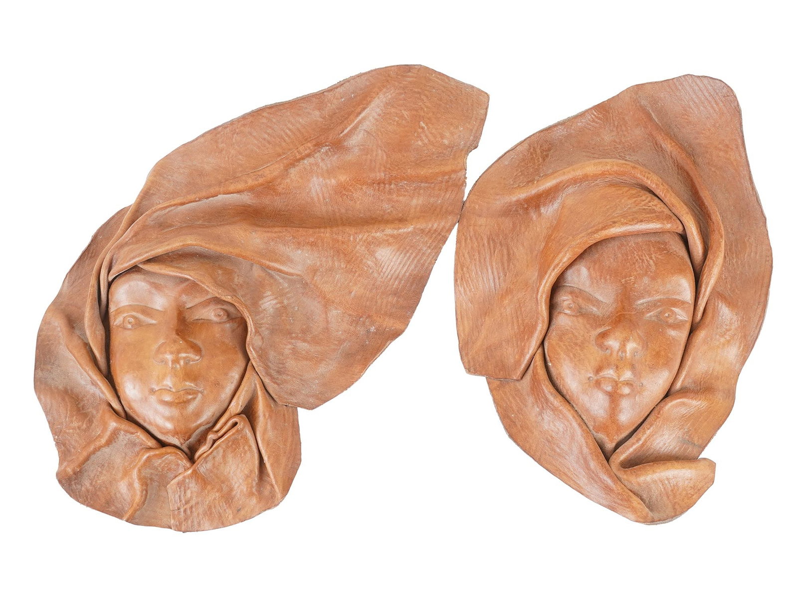 VINTAGE HAITIAN FOLK ART LEATHER FACE MASKS: A pair of vintage Haitian hand-crafted molded leather female faces. This kind of art can be found across the Caribbean and in Mexico. The pieces serve as wall hangings. There are suspensions on the ba