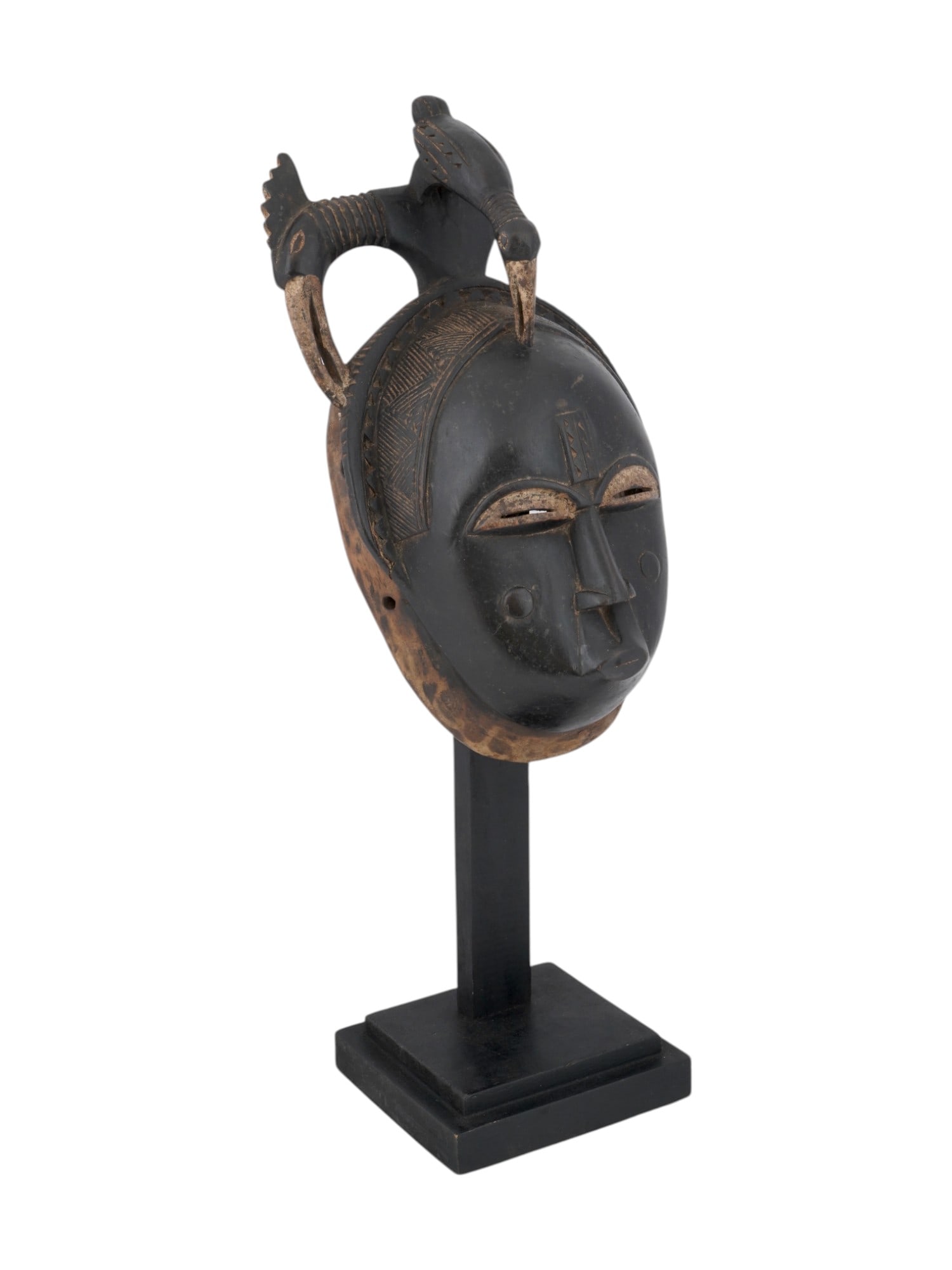 CENTRAL AFRICAN BAULE PEOPLE CARVED WOODEN MASK: A Central African Ivory Coast hand carved wooden mask of Baule people. The mask is modeled with narrow eyes, a small mouth, and a high, complex headdress. The headdress includes a wide headband to whi