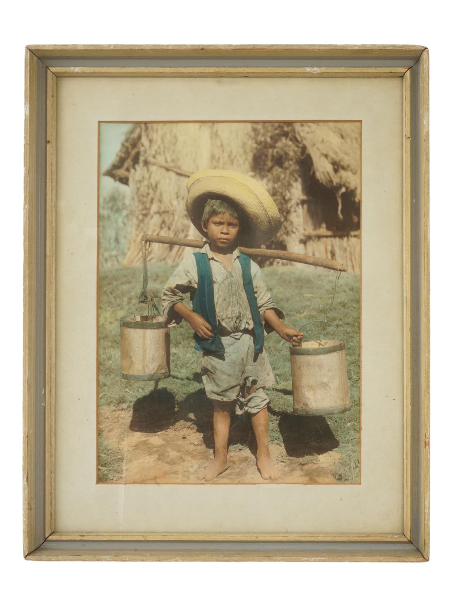 VINTAGE COLOR ETHNOGRAPHIC PHOTOGRAPH BOY WITH BUCKETS: A vintage color photograph featuring a young boy carrying two buckets, set against the backdrop of a traditional house. The boy, dressed in authentic attire, stands in a moment of candid activity, whi