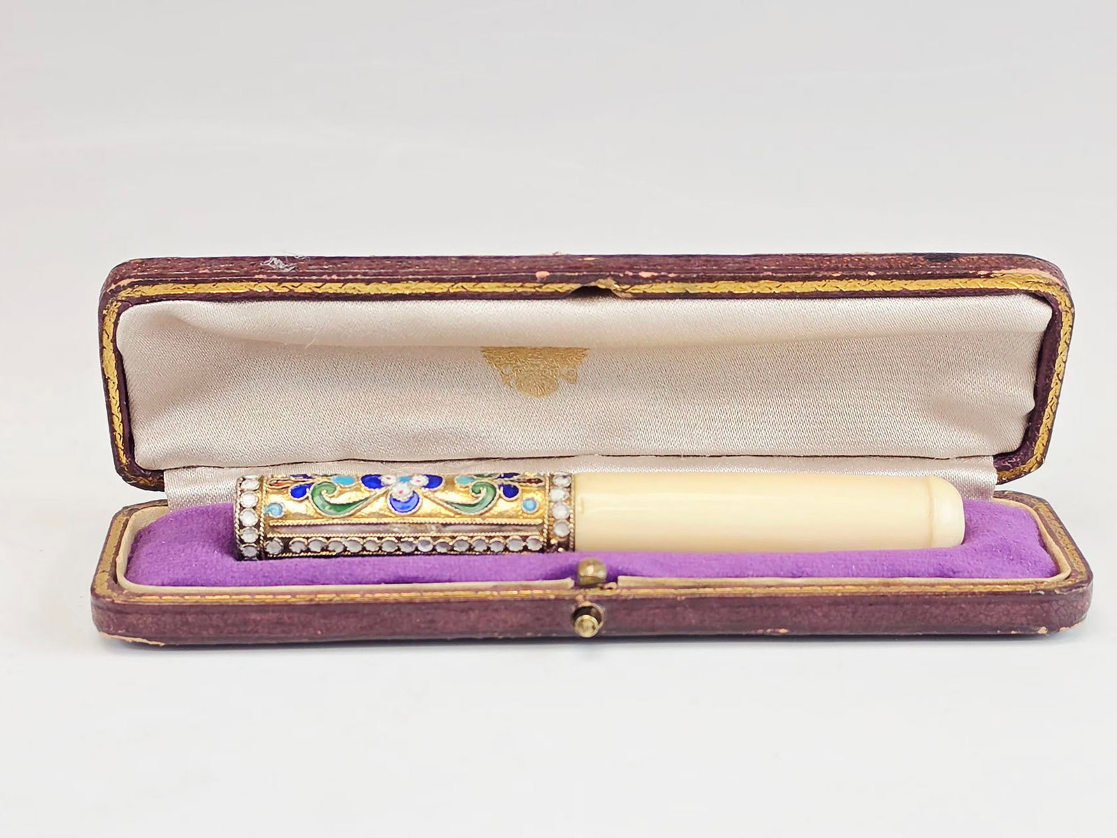 RUSSIAN GILT SILVER CLOISONNE ENAMEL CIGARETTE HOLDER: An early 20th-century Russian gilt silver cigarette holder or mouthpiece richly decorated with vibrant cloisonne enamel in deep blue, green, and white tones over the textured ground. The refined symme