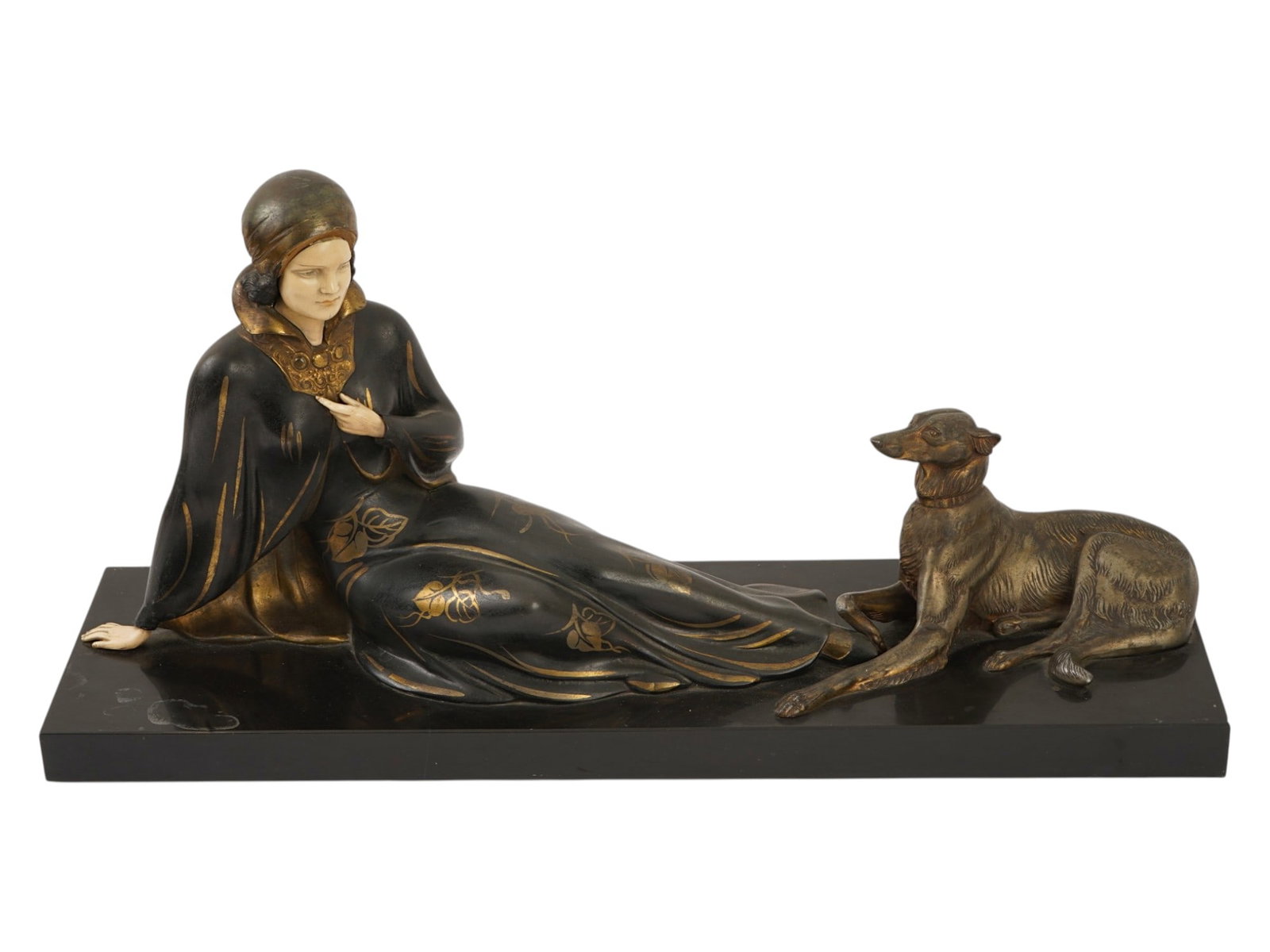 ART DECO COMPOSITE FIGURE ON A BLACK MARBLE BASE: This Art Deco style figurative group depicts a seated woman in an elegant, flowing gown and cape, gazing toward a reclining hound. Rendered in cold-painted spelter with a composite or ivorine face, th