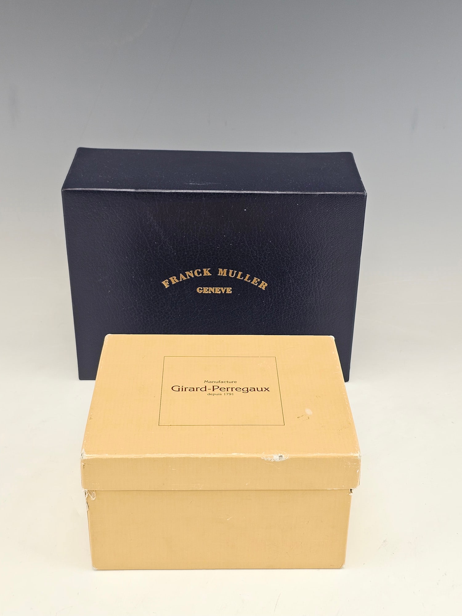 FRANCK MULLER AND GIRARD PERREGAUX WATCH BOXES: A lot of two original presentation boxes for Franck Muller and Girard Perregaux watches. The Franck Muller set includes a high-gloss burl wood box with a black upholstered interior and watch cushion,