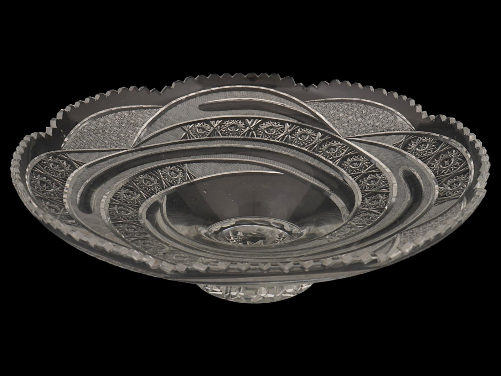 VINTAGE FOOTED SWIRL CUT GLASS DESIGN CRYSTAL BOWL: A circular form clear crystal fruit or candy bowl. The bowl features a dynamic molded swirl pattern originating from the center and extending to a scalloped, wavy rim. The exterior surface is textured