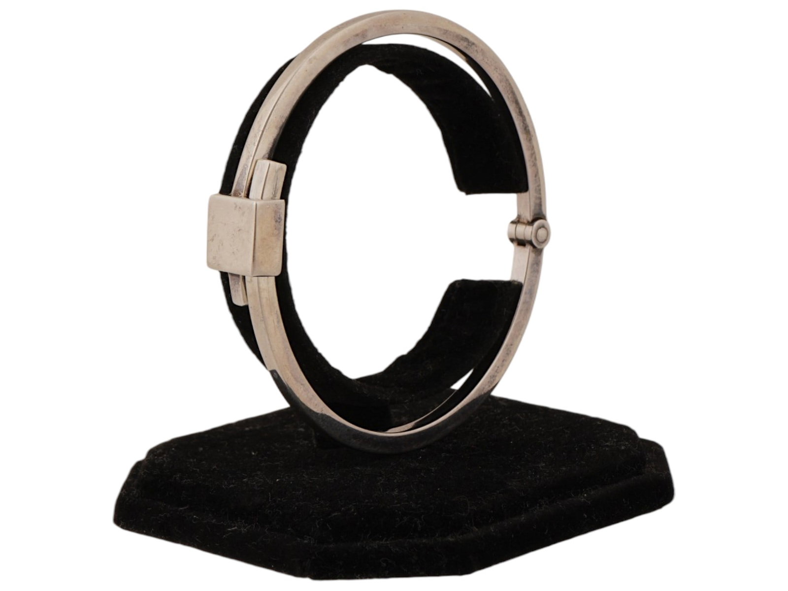 ITALIAN GUCCI STERLING SILVER HINGED BANGLE BRACELET: A Gucci hinged bangle bracelet crafted from polished 925 sterling silver and features a minimalist, architectural design. The piece is centered by a prominent square shaped plaque that serves as a dec