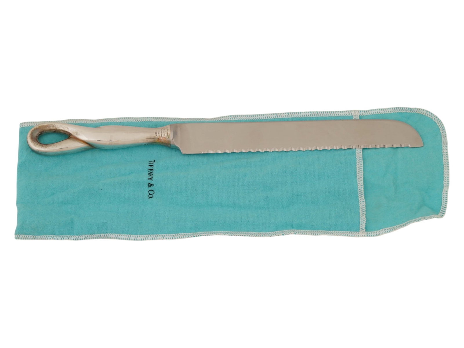TIFFANY CO ELSA PERETTI ST SILVER BREAD KNIFE 1984: A Tiffany and Co sterling silver serrated bread knife of Padova series. The item is designed by Elsa Peretti and adorned with a twisted loop on the handle. Marked with a brand logo, a T and Co. sterli
