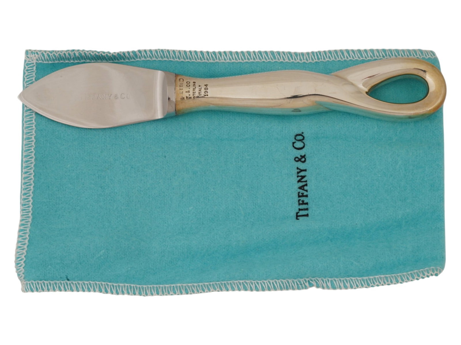 TIFFANY CO ELSA PERETTI ST SILVER CHEESE KNIFE 1984: A Tiffany and Co sterling silver parmesan cheese knife of Padova series. The item is designed by Elsa Peretti and adorned with a twisted loop on the handle. Marked with a brand logo, a T and Co. sterl