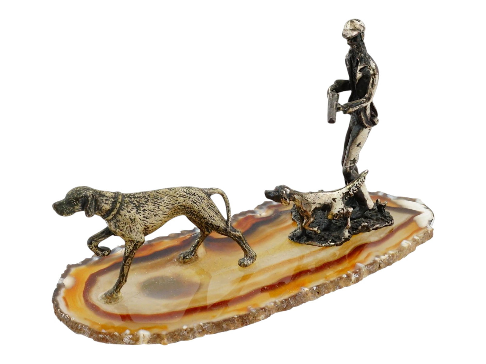 VINTAGE SILVER SCULPTURE HUNTER AND DOGS ON STONE BASE: A vintage hunting diorama sculpture featuring a hunter with two pointing dogs in a traditional sporting scene. The figures are cast in silver with detailed surfaces and mounted on a polished stone bas