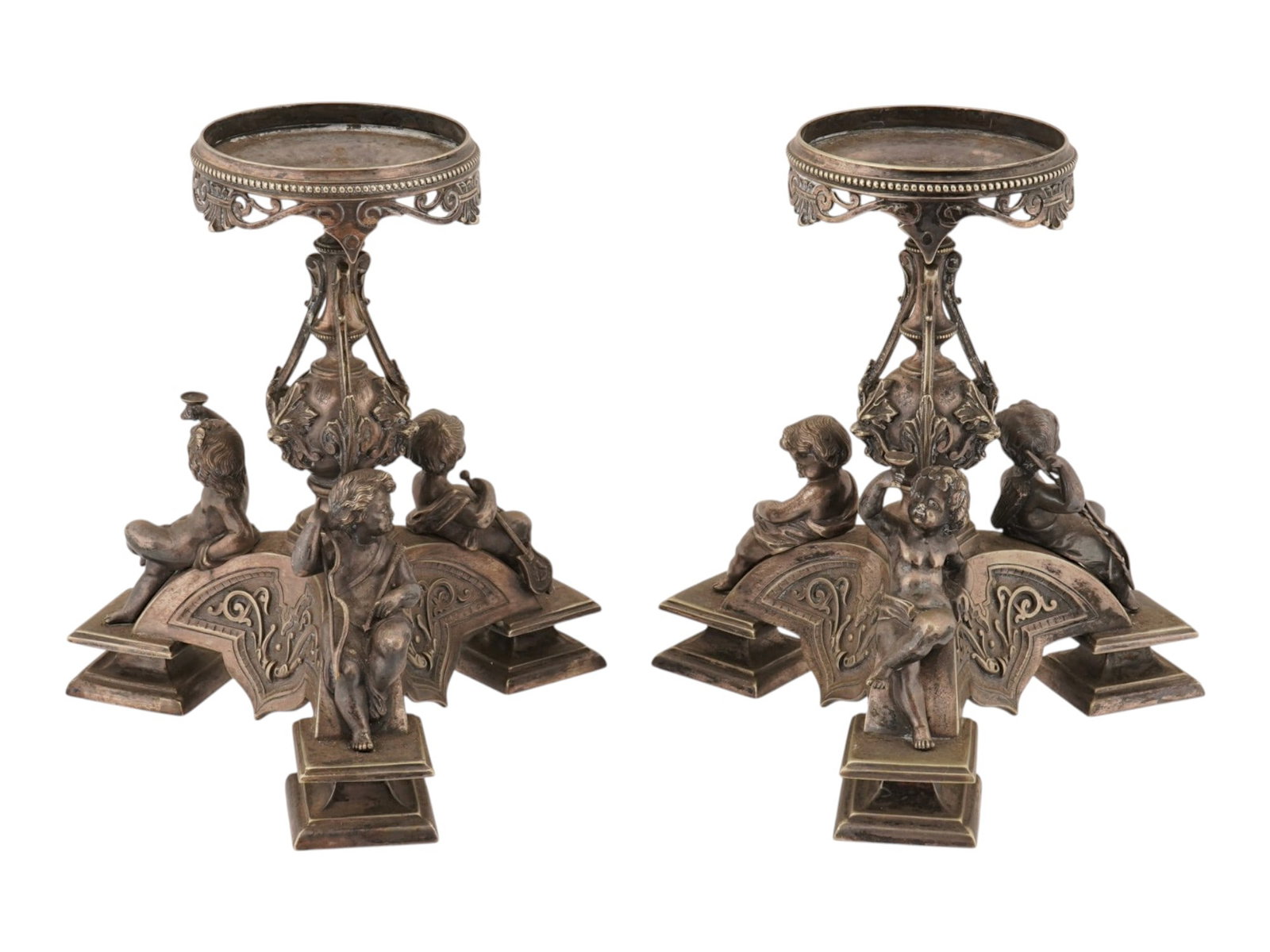 PAIR OF ANTIQUE FRENCH CHERUBS METAL CANDLESTICKS: A pair of antique French metal candlesticks or tazza stands featuring detailed putti figures. The wares are crafted from cast metal with a dark, patinated finish, featuring a tripartite base supported