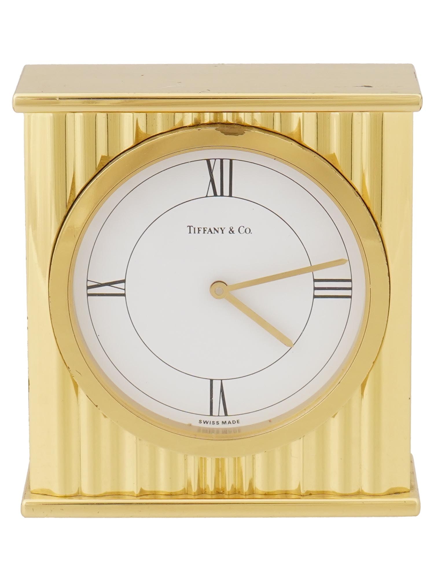 AMERICAN TIFFANY AND CO SWISS MADE BRASS DESK CLOCK: A vintage American brass desk clock manufactured by Tiffany and Co. The clock features a white enamelled dial with Roman numeral quarter hours and a quartz movement. The case is made in an Art Deco ri