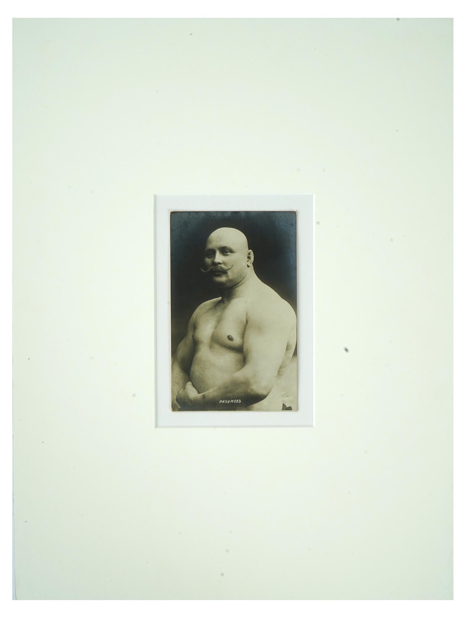 ANTIQUE RUSSIAN PORTRAIT PHOTO OF FAMOUS WRESTLER: An antique Russian post card with a black and white photograph, depicting a studio portrait of Razumov, a Russian wrestler and athlete. Circa: early 20th century. Titled, lower to the center. The phot